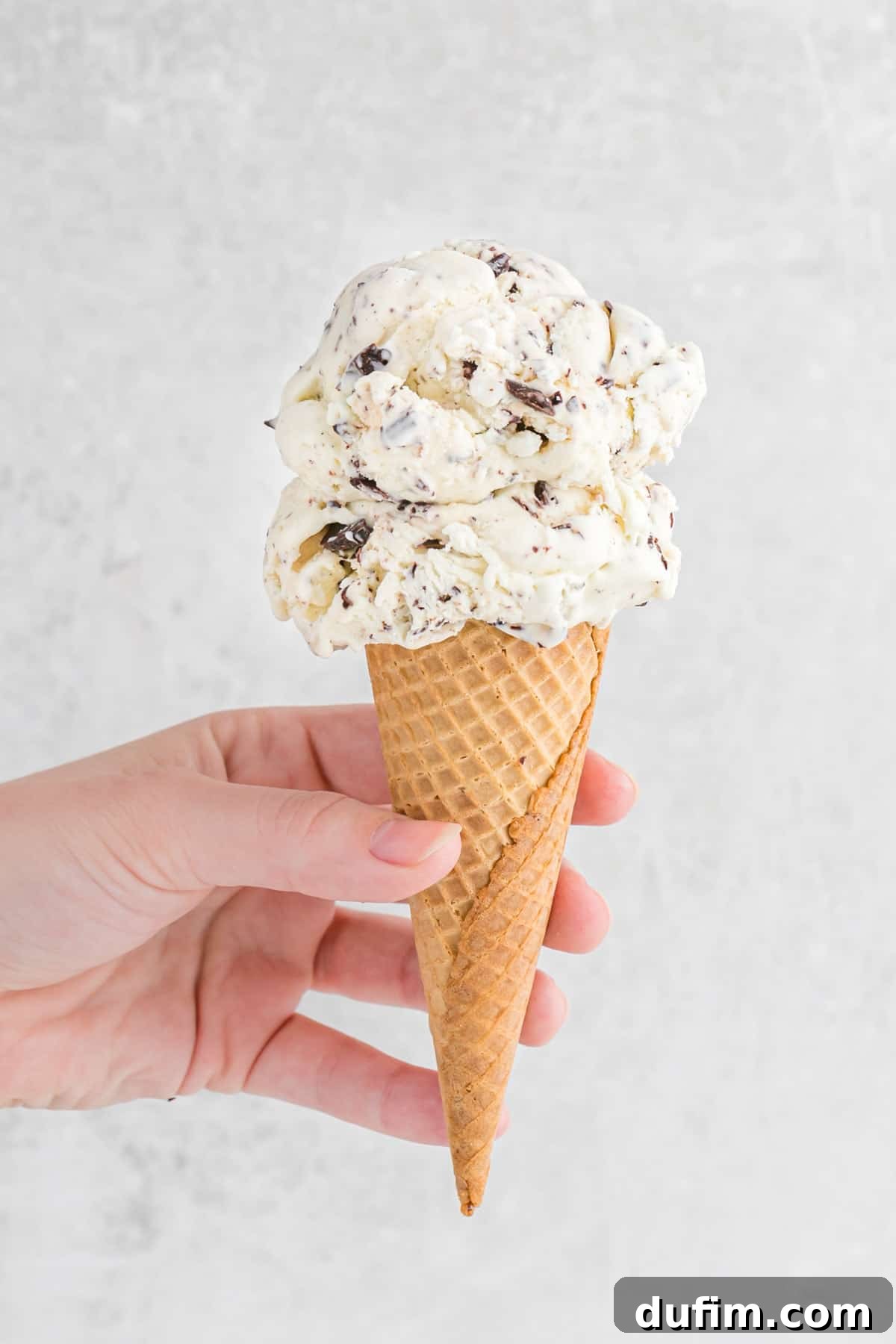 A hand holding an ice cream cone with two scoops of chocolate chip ice cream, against a vibrant background.