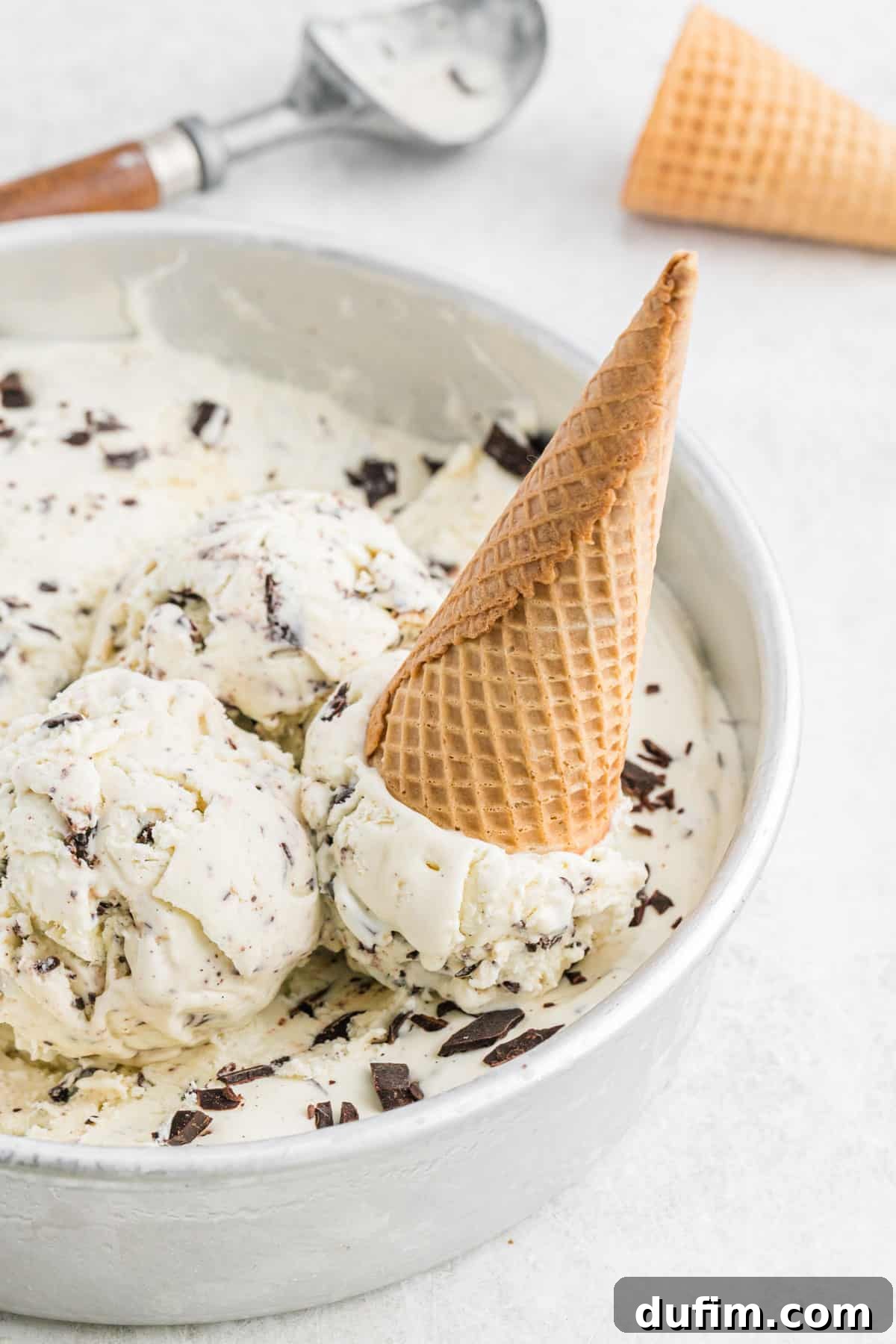 No-churn ice cream presented in a round pan with an ice cream cone resting beside it, ready for serving.