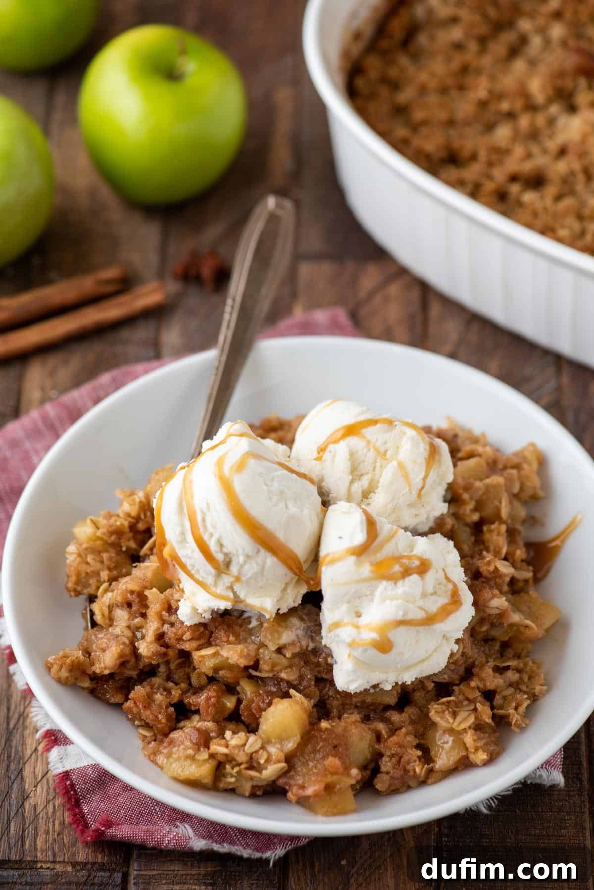 A close-up shot of a single serving of caramel apple crisp in a small white bowl, adorned with a scoop of vanilla ice cream and a luxurious drizzle of extra caramel sauce, highlighting the dessert's indulgence.