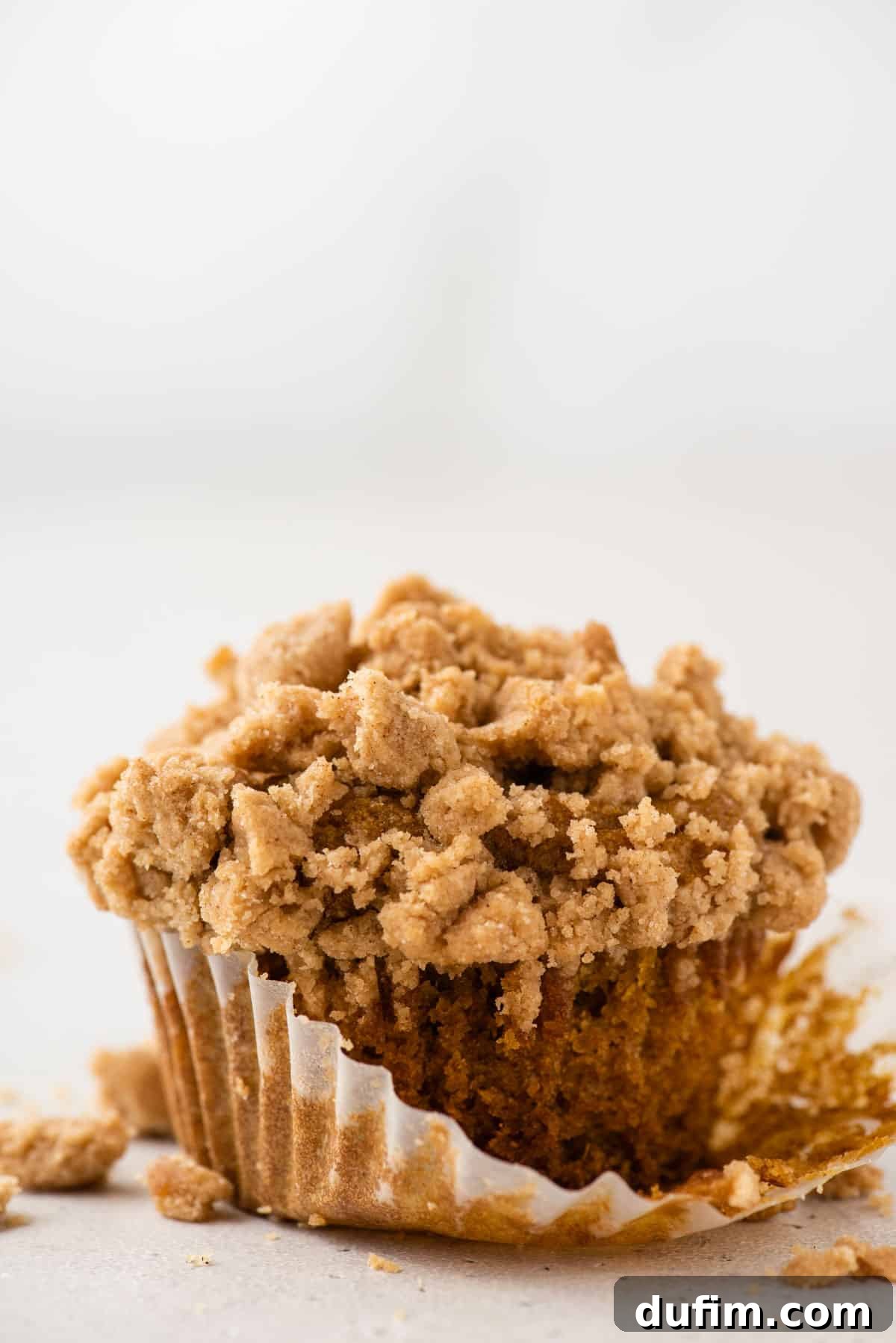Autumn Spiced Gluten-Free Pumpkin Streusel Muffins 5 a single gluten free pumpkin muffin with liner half removed on white background