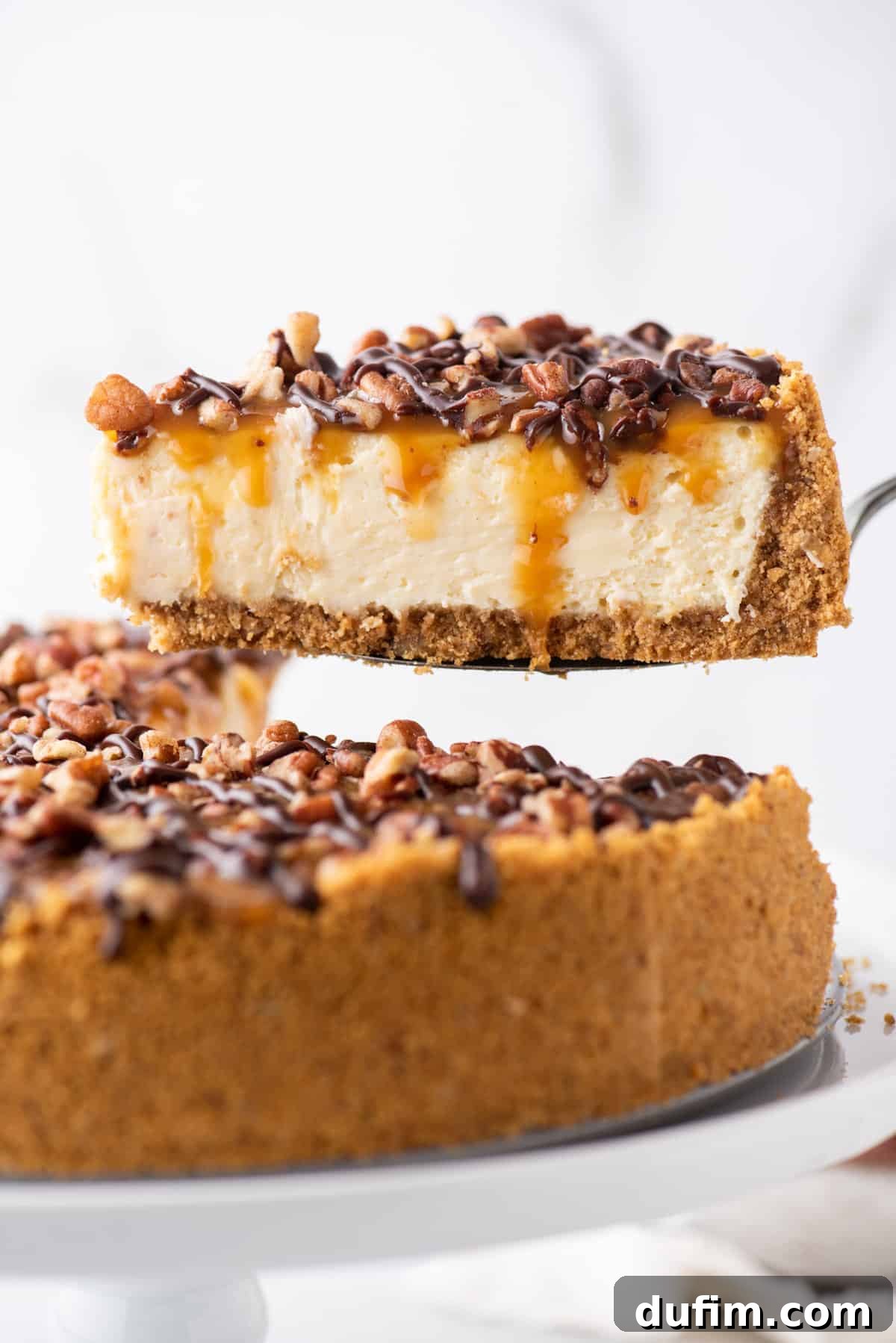 slice of turtle cheesecake with graham cracker crust on metal spatula