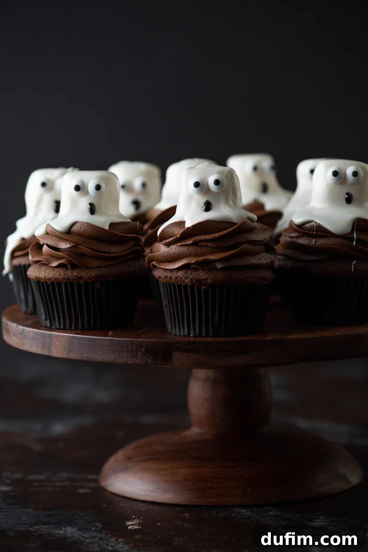 Ghost Cupcakes - Spooky Halloween Fun Delicious ghost cupcakes arranged artfully on a rustic wooden cake stand, set against a dark, atmospheric background, perfect for a Halloween party dessert display