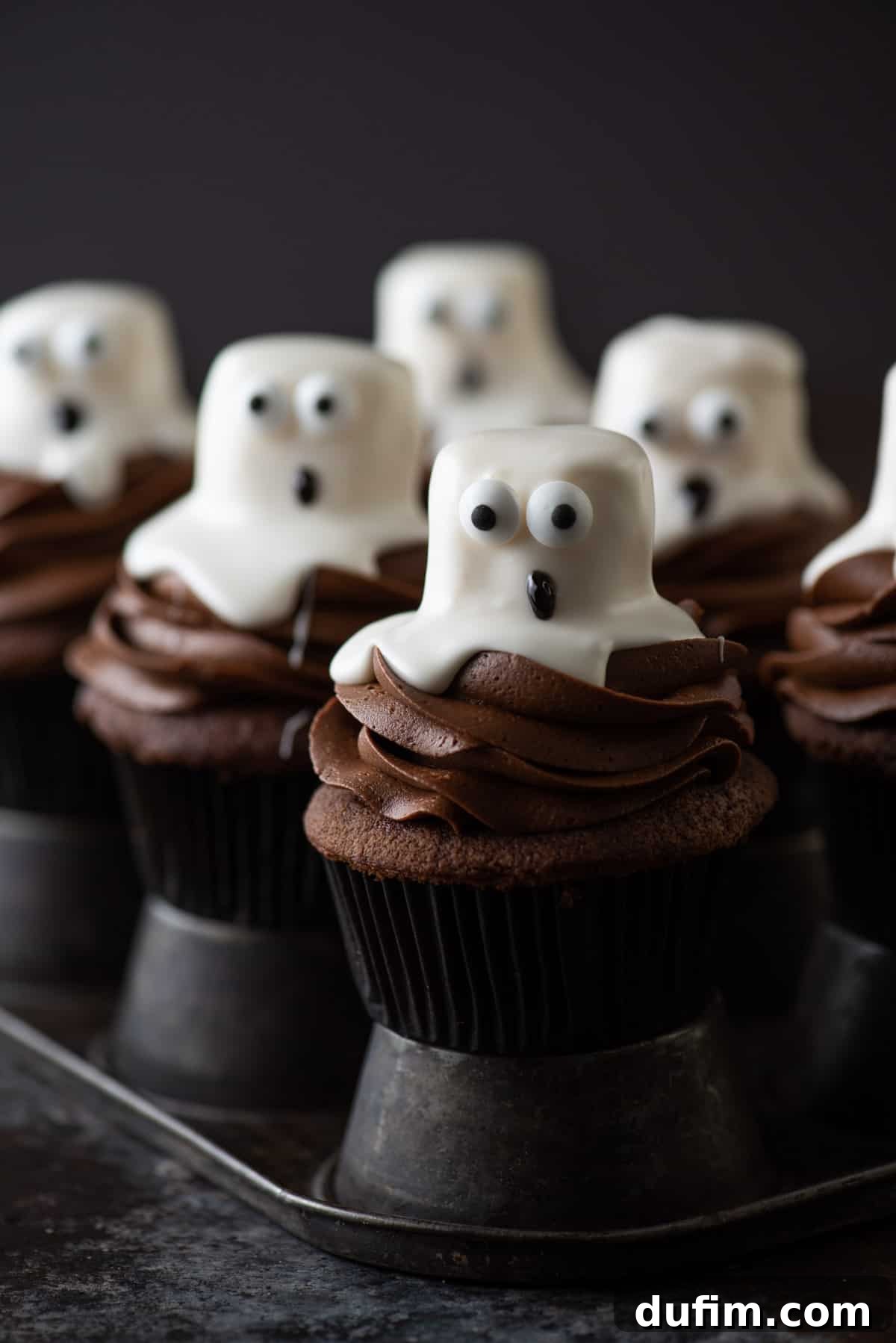 Cooling Chocolate Cupcakes for Ghosts Freshly baked chocolate ghost cupcakes cooling in a metal muffin pan, awaiting their delicious frosting and whimsical ghost decorations