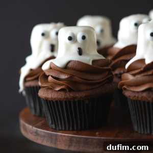 Ghost Cupcakes Recipe Thumbnail Ghost cupcakes topped with rich chocolate frosting and white marshmallow ghost decorations, complete with candy eyes and drawn mouths, artfully arranged on a wooden platter.
