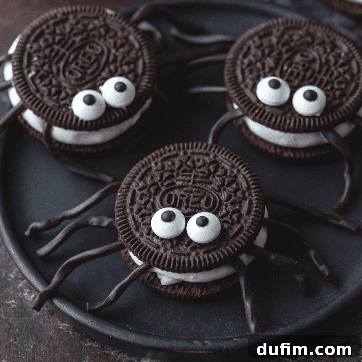 Easy No-Bake Oreo Spiders for Halloween Three Oreo spiders on a black plate, showcasing their candy eyes and licorice legs.