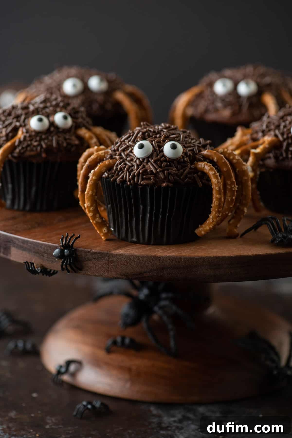 Halloween Spider Cupcakes: A festive and fun dessert for all ages. Halloween spider cupcakes featuring chocolate frosting, pretzel legs, and candy eyes, displayed on a elegant brown cake stand.