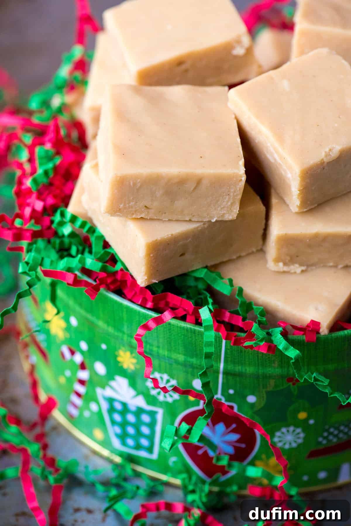 A festive Christmas tin filled with slices of microwave peanut butter fudge, nestled among red and green crinkle paper, ready for gifting or storage.