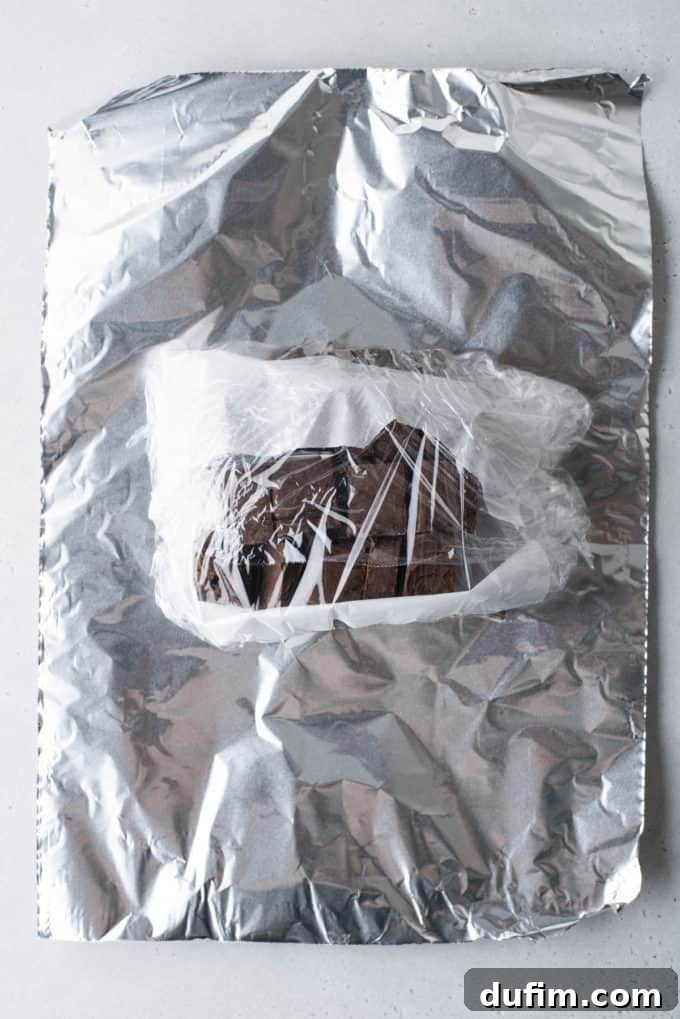 Chocolate fudge, already wrapped in plastic, is now placed on a sheet of aluminum foil, ready for its second layer of protection against freezer burn.