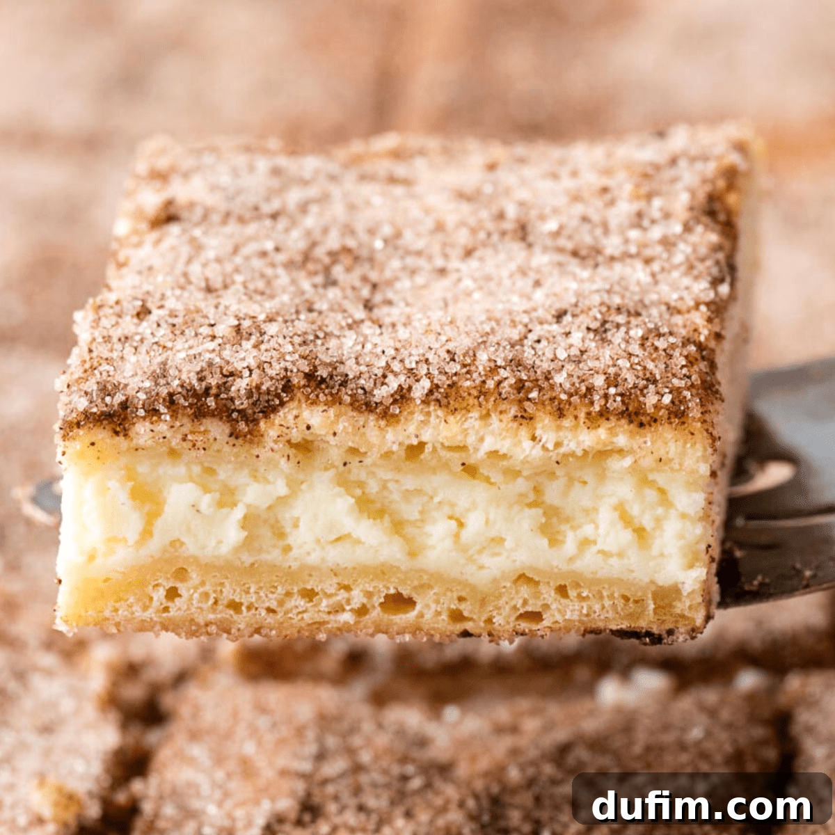 With a buttery, flaky crust, cinnamon sugar topping, and tangy cheesecake filling, this Churro Cheesecake is easy to make & ridiculously good. A churro cheesecake bar on a spatula, showcasing its layers and cinnamon sugar topping