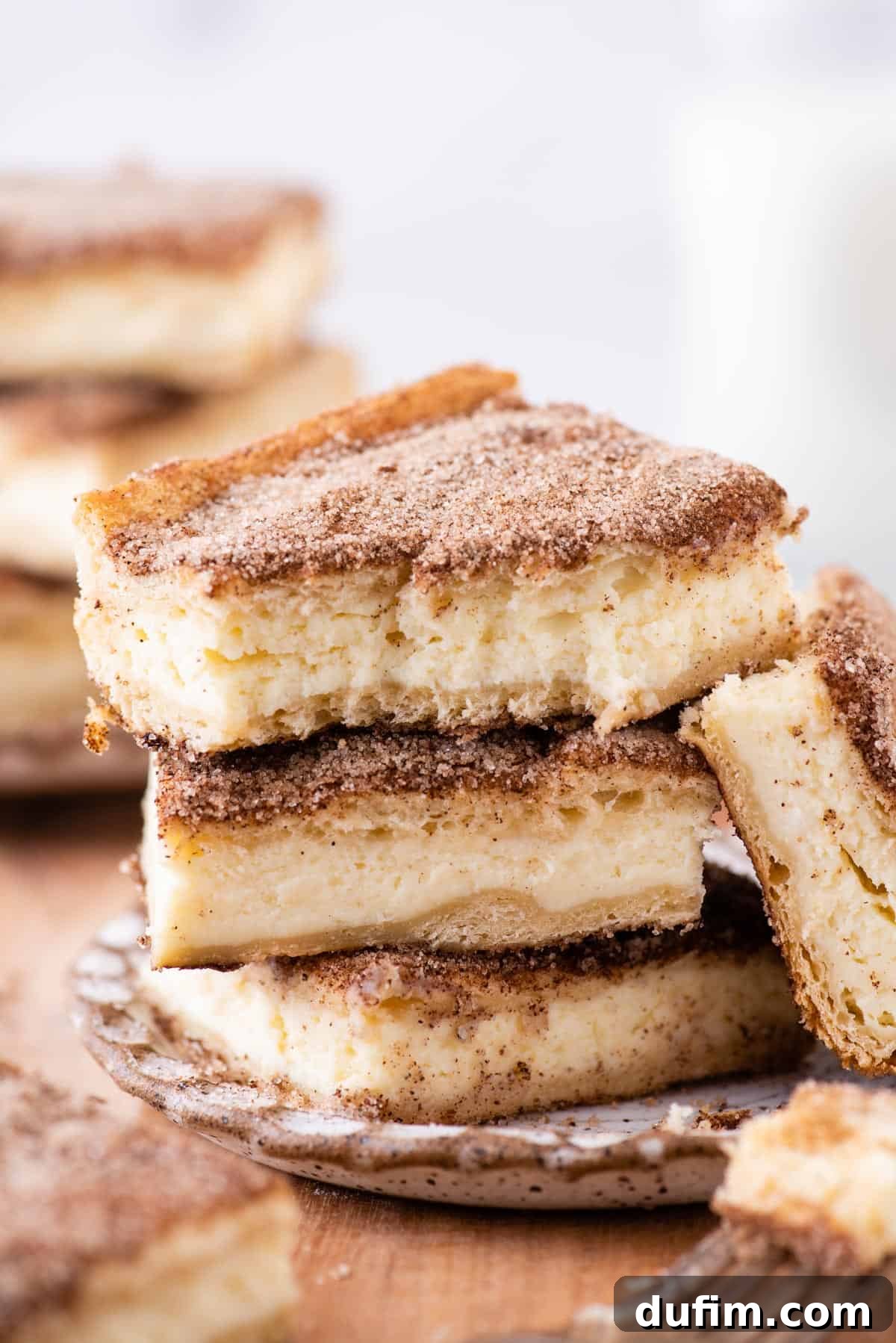 With a buttery, flaky crust, cinnamon sugar topping, and tangy cheesecake filling, this Churro Cheesecake is easy to make & ridiculously good. Three churro cheesecake bars stacked neatly on each other, showing the layered texture