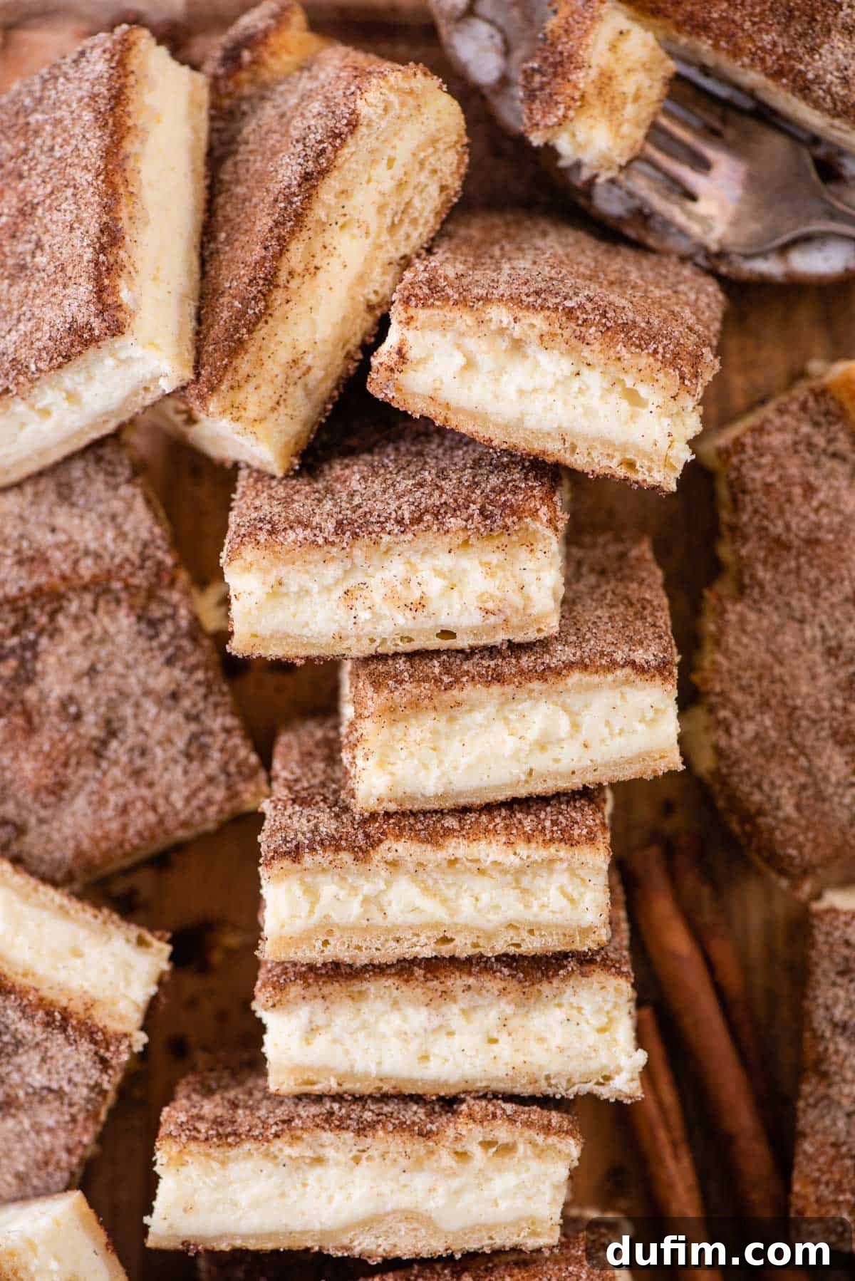 With a buttery, flaky crust, cinnamon sugar topping, and tangy cheesecake filling, this Churro Cheesecake is easy to make & ridiculously good. Overhead view of perfectly cut churro cheesecake bars, showcasing their golden topping and creamy filling