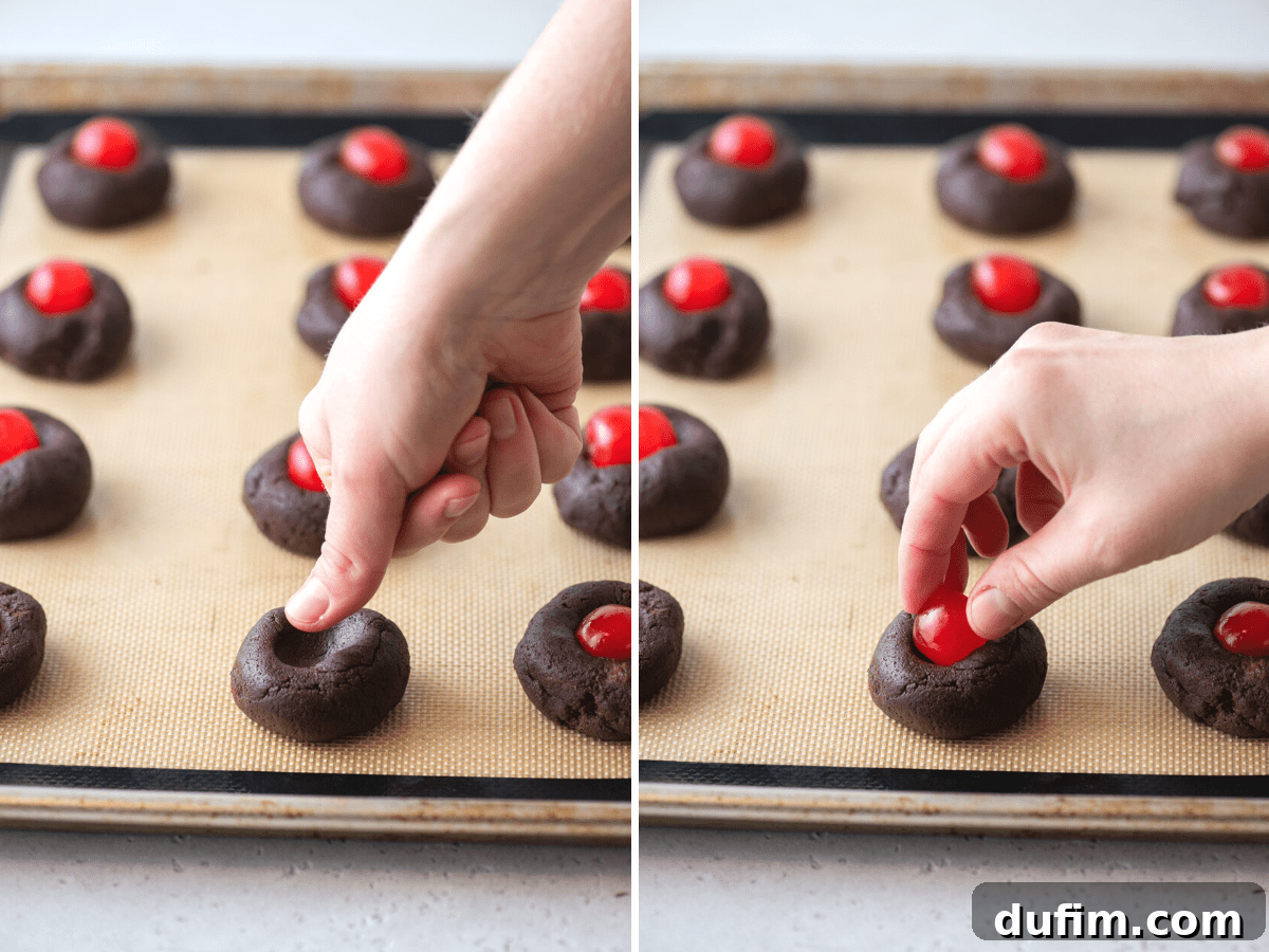 A thumb creating an indent in chocolate cookie dough on a baking sheet, followed by a maraschino cherry being placed in the center.