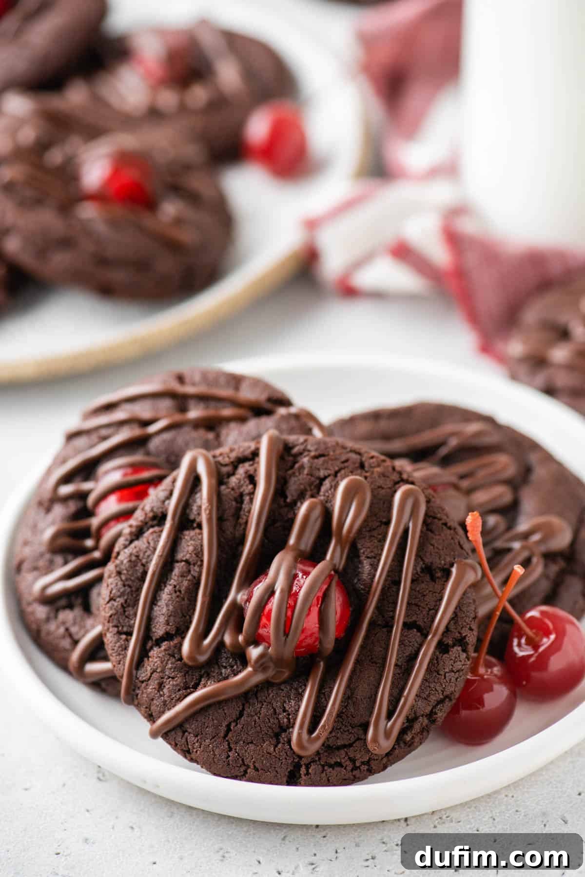 A stack of three chocolate cherry cookies on a small white plate, ready for a delicious treat.