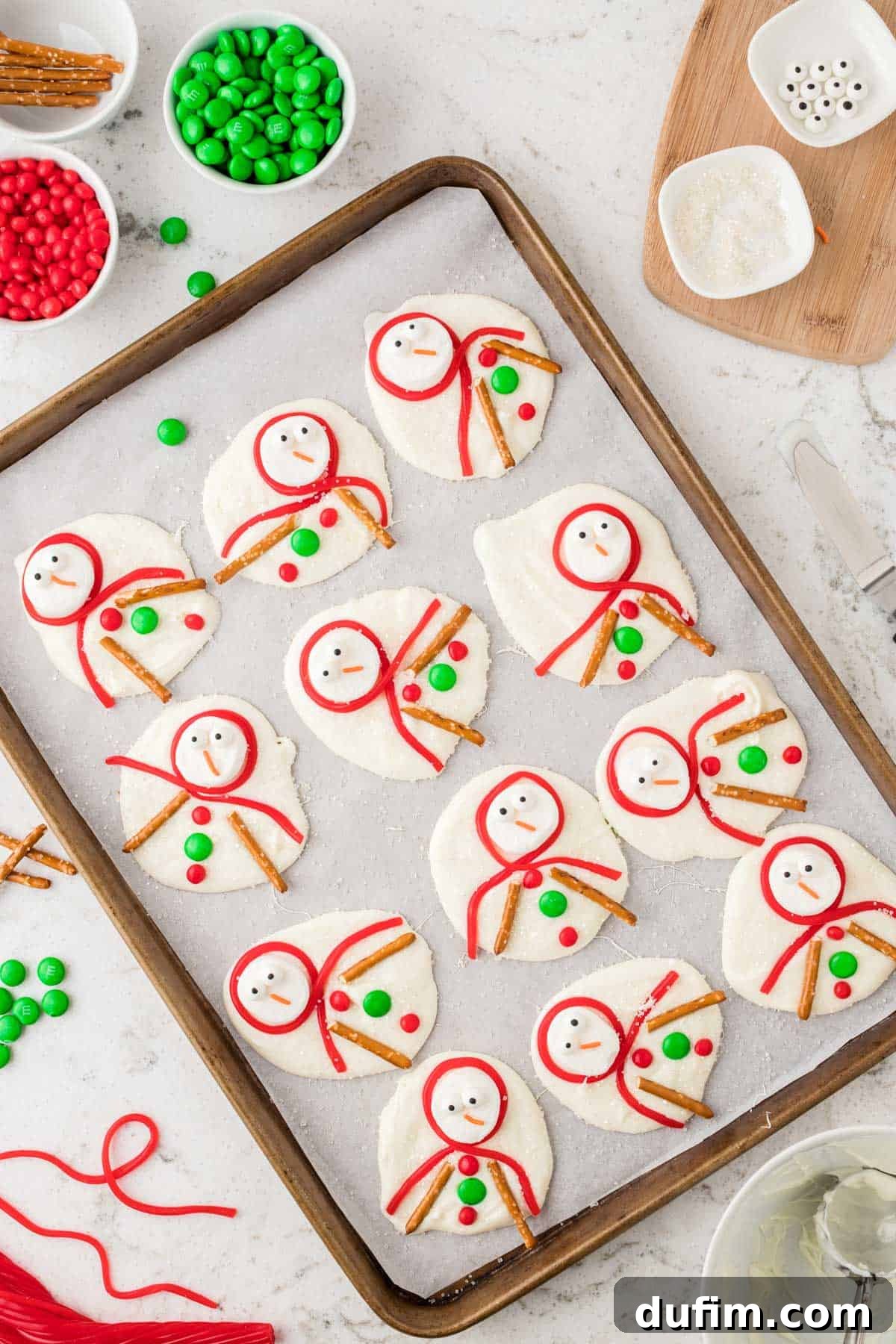 Completed melted snowman bark on parchment paper, featuring all decorations including candy buttons and pretzel arms, creating a whimsical winter scene.