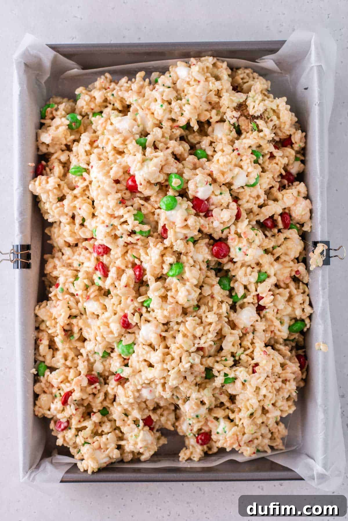 The vibrant Christmas Rice Krispie treat mixture carefully transferred into a prepared baking dish.