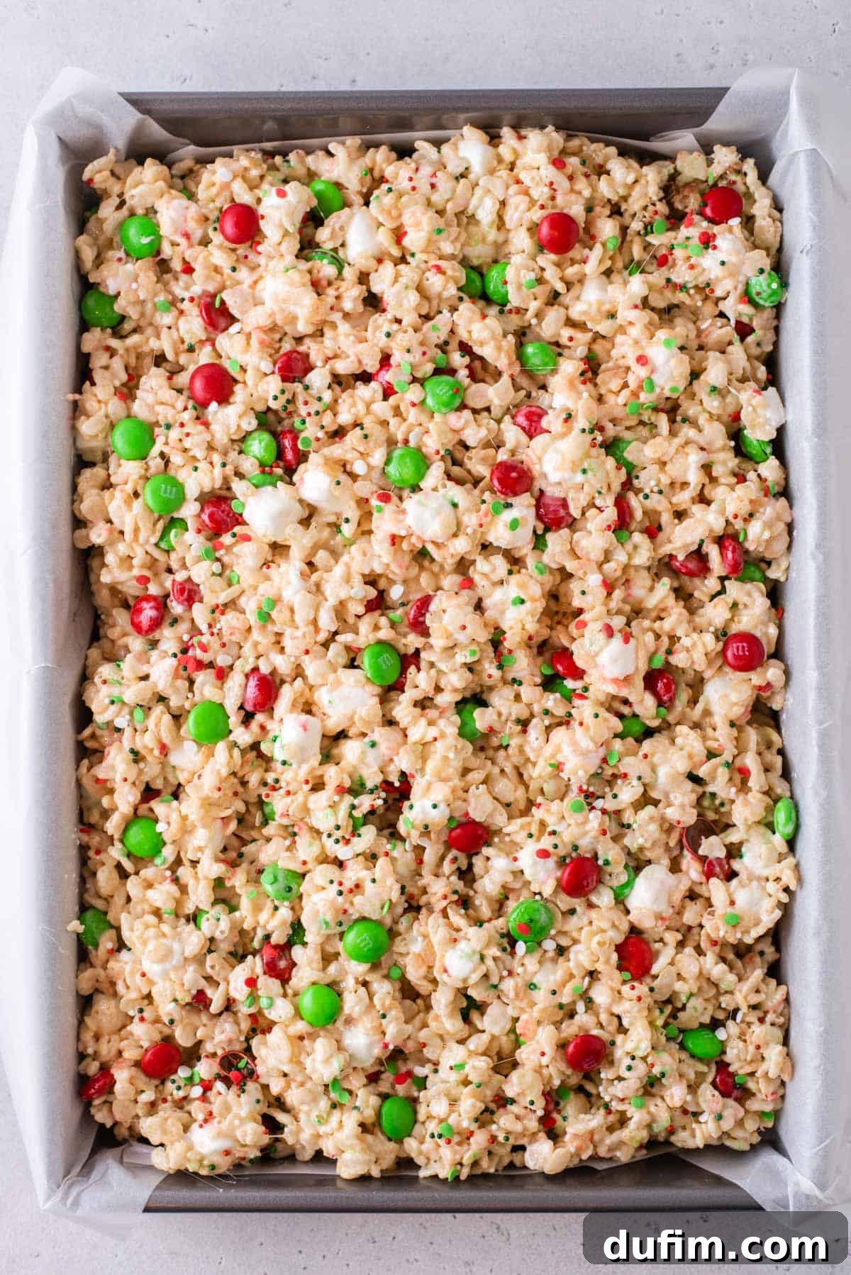 Christmas Rice Krispie treats gently pressed into a baking dish, showcasing their even layer and vibrant holiday colors.