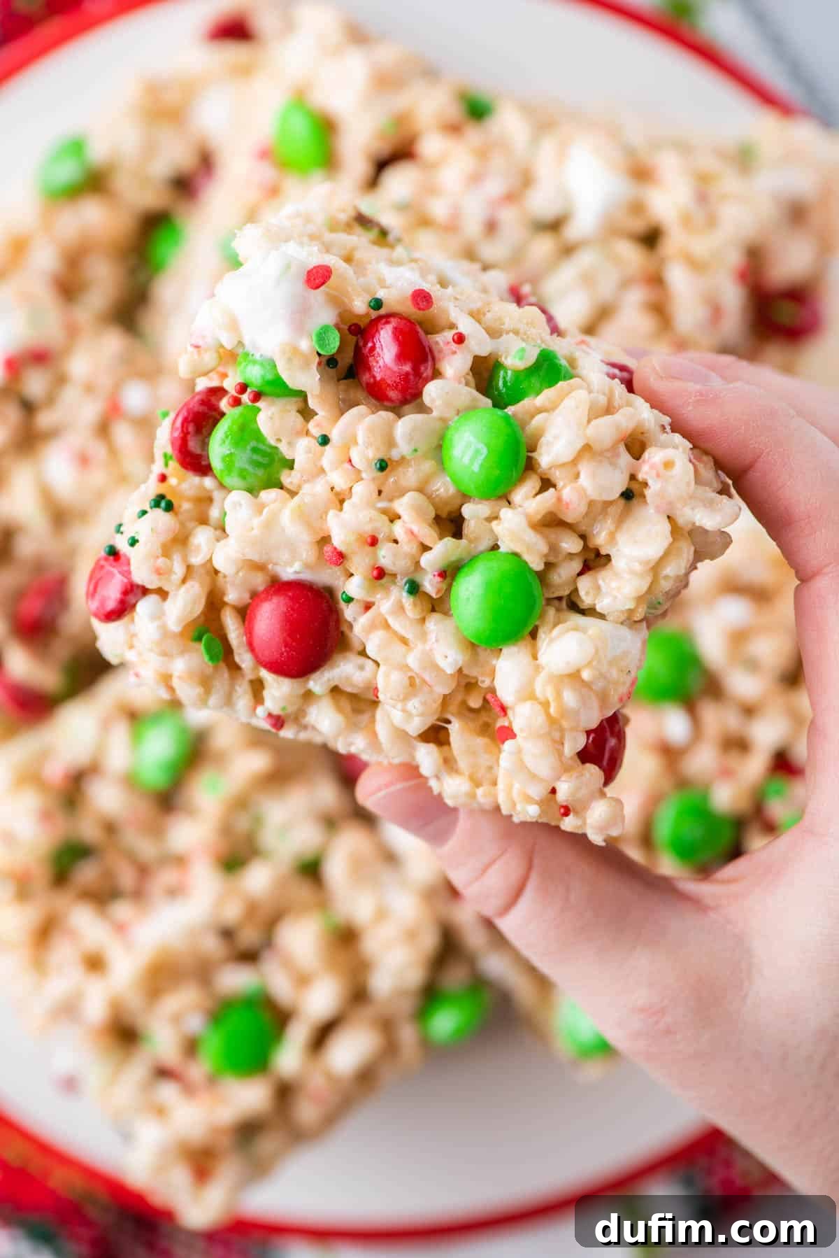A hand gently holding a single, perfect holiday Rice Krispie treat, showcasing its texture and vibrant M&Ms.