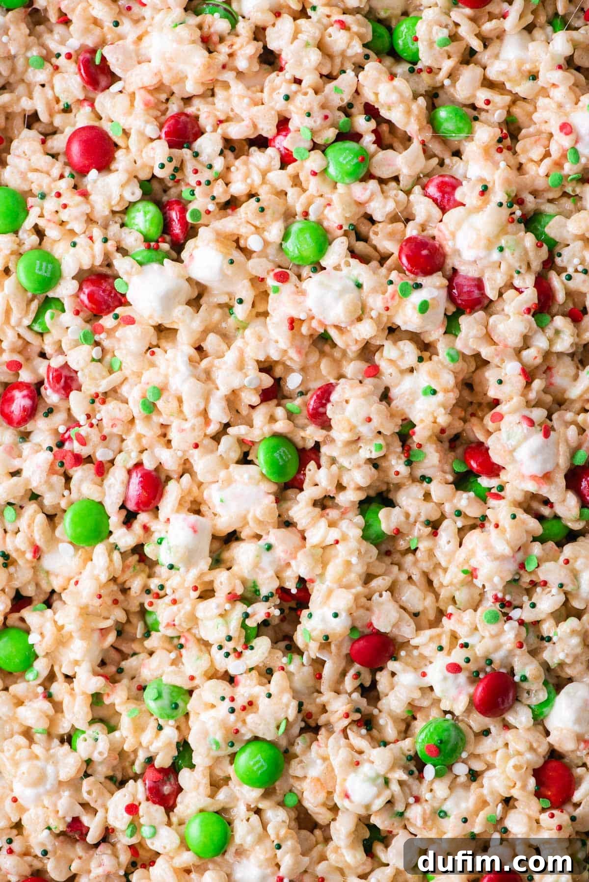 Close-up shot of a stack of festive holiday Rice Krispie treats, showcasing their soft texture and colorful M&Ms and sprinkles.