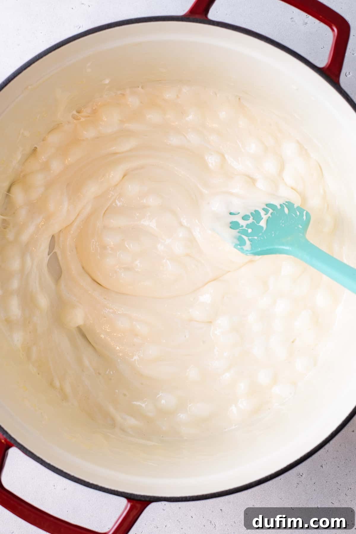 A blue spatula stirring melting mini marshmallows and butter in a pot, creating a smooth, gooey mixture.