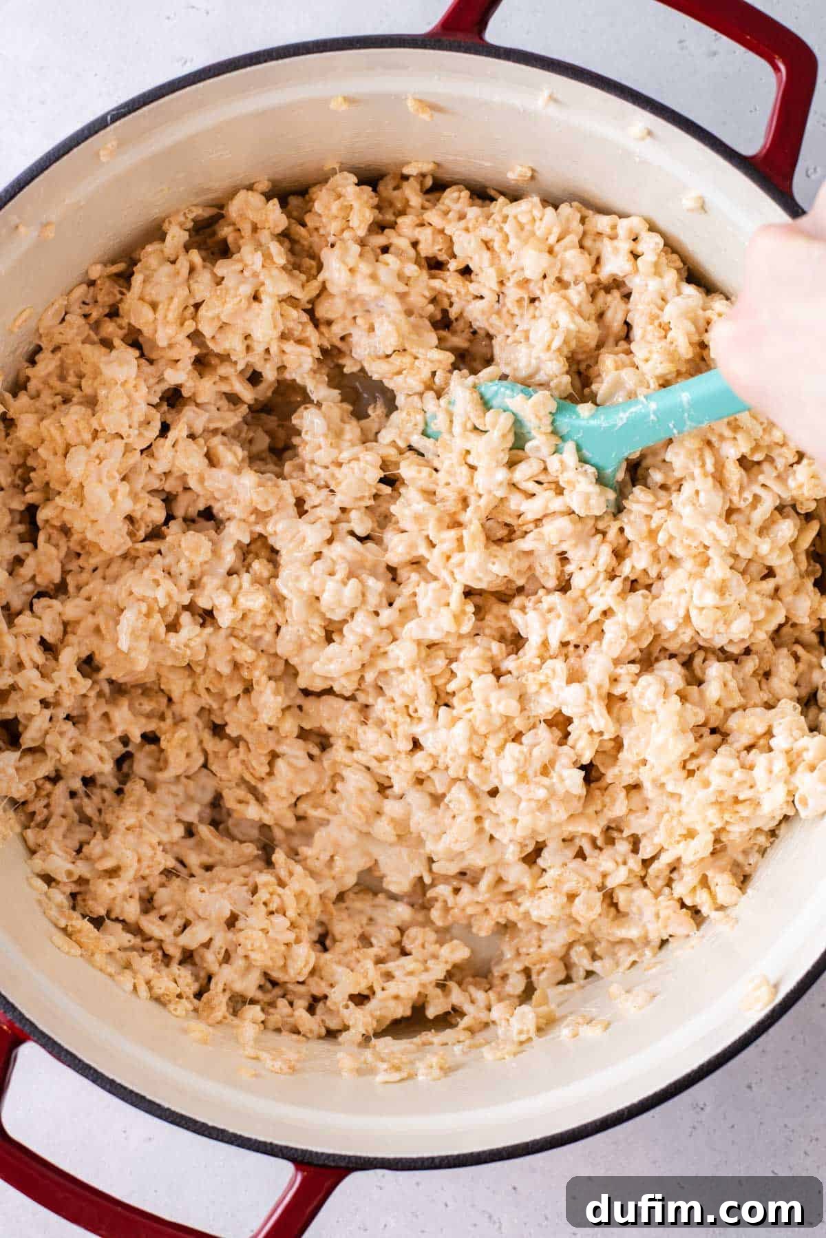 A blue spatula mixing the Rice Krispie treat mixture, showing the cereal evenly coated with marshmallow.