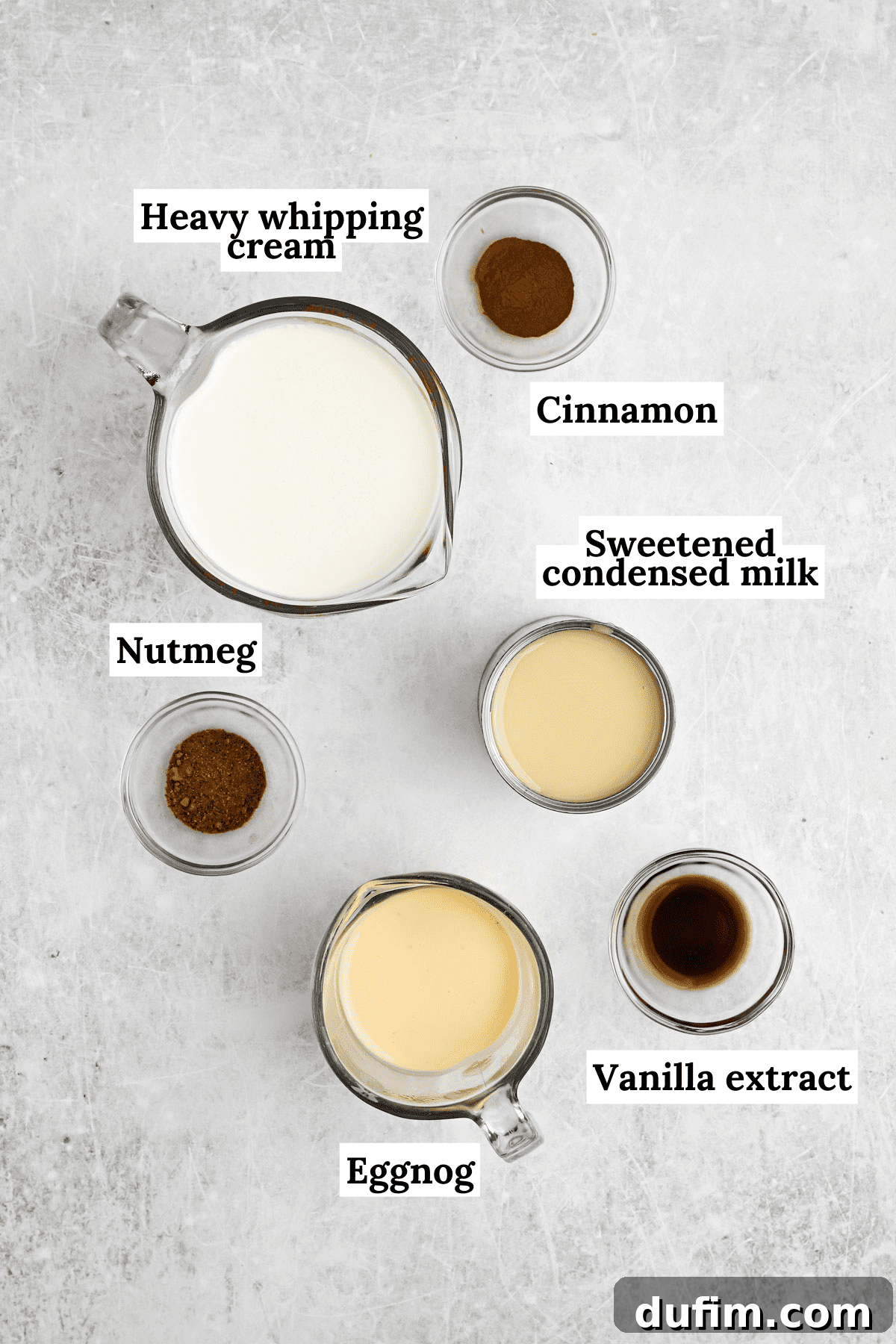 Made with only 6 ingredients, Eggnog Ice Cream is rich, creamy, and perfectly spiced. Perfect for the holidays, with 10 minutes of prep! An overhead view of the six simple ingredients for no-churn eggnog ice cream, including heavy cream, eggnog, spices, vanilla extract, and sweetened condensed milk, neatly arranged on a counter.