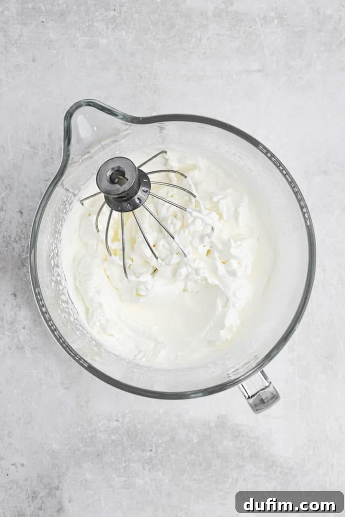 Creamy Homemade Eggnog Ice Cream 2 Heavy whipping cream being beaten in a glass mixing bowl, transforming into stiff peaks.
