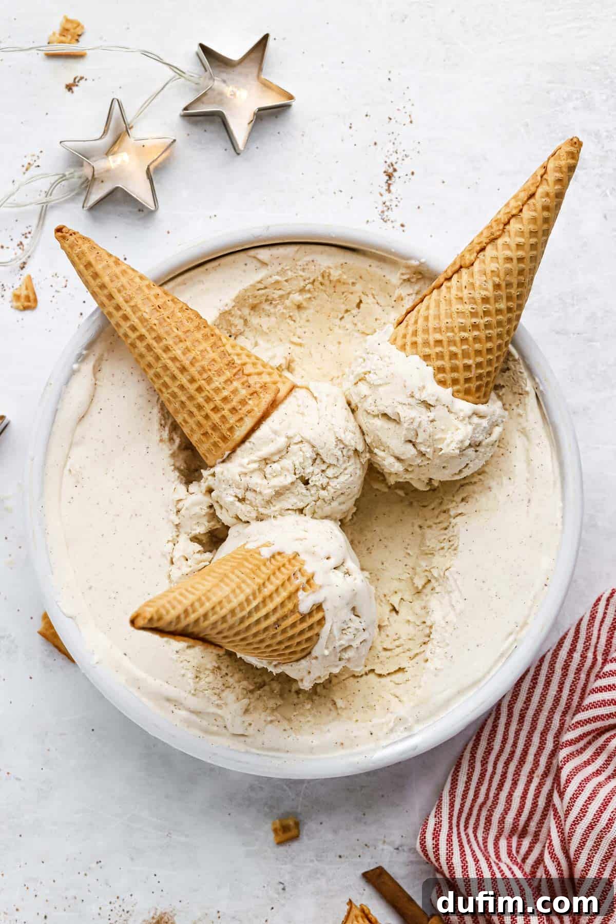 Made with only 6 ingredients, Eggnog Ice Cream is rich, creamy, and perfectly spiced. Perfect for the holidays, with 10 minutes of prep! Three waffle cones filled with scoops of eggnog ice cream, resting on top of a loaf pan brimming with the frozen dessert.