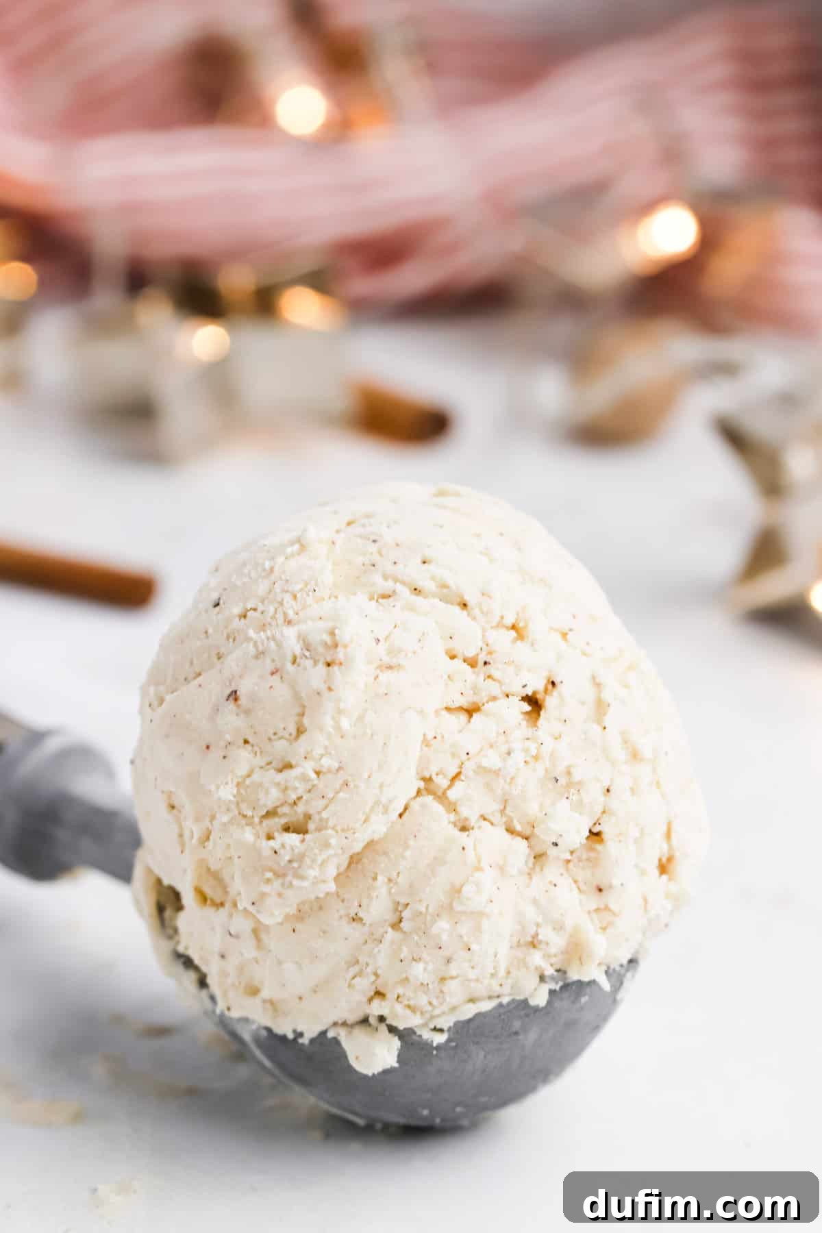 Made with only 6 ingredients, Eggnog Ice Cream is rich, creamy, and perfectly spiced. Perfect for the holidays, with 10 minutes of prep! A scoop of eggnog ice cream sitting on a wooden table, featuring its smooth texture and readiness to be served.