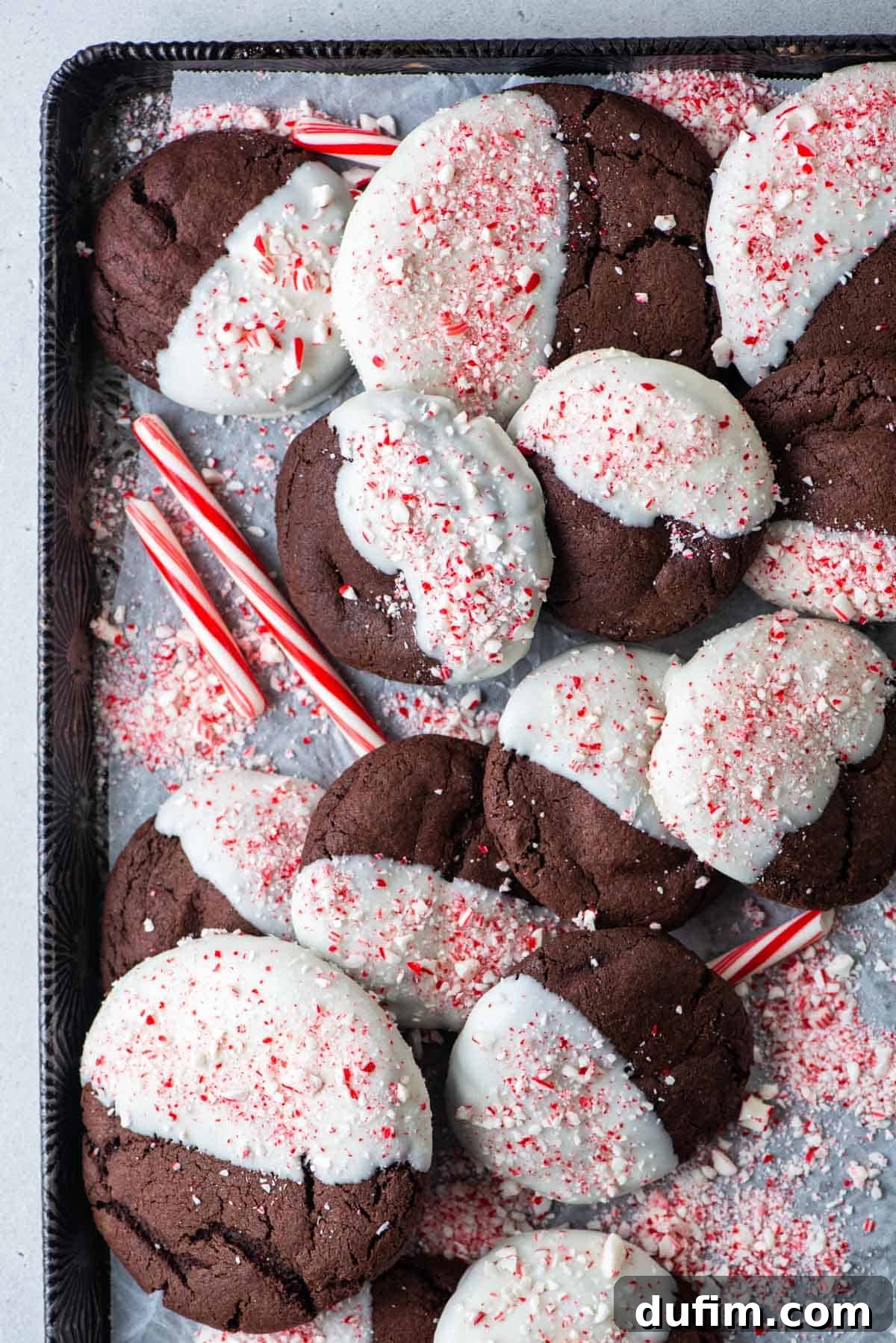 These Chocolate Candy Cane Cookies feature soft, chewy chocolate cookies dipped in white chocolate and sprinkled with crushed candy canes. Overhead view of several perfectly arranged chocolate candy cane cookies, highlighting their festive toppings and rich color.