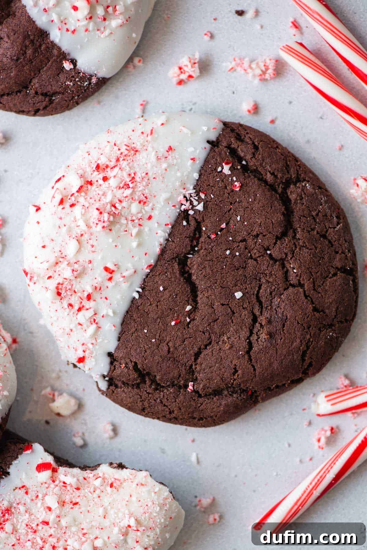 These Chocolate Candy Cane Cookies feature soft, chewy chocolate cookies dipped in white chocolate and sprinkled with crushed candy canes. Overhead view of a single chocolate candy cane cookie, perfectly round and adorned with a white chocolate dip and crushed candy canes.