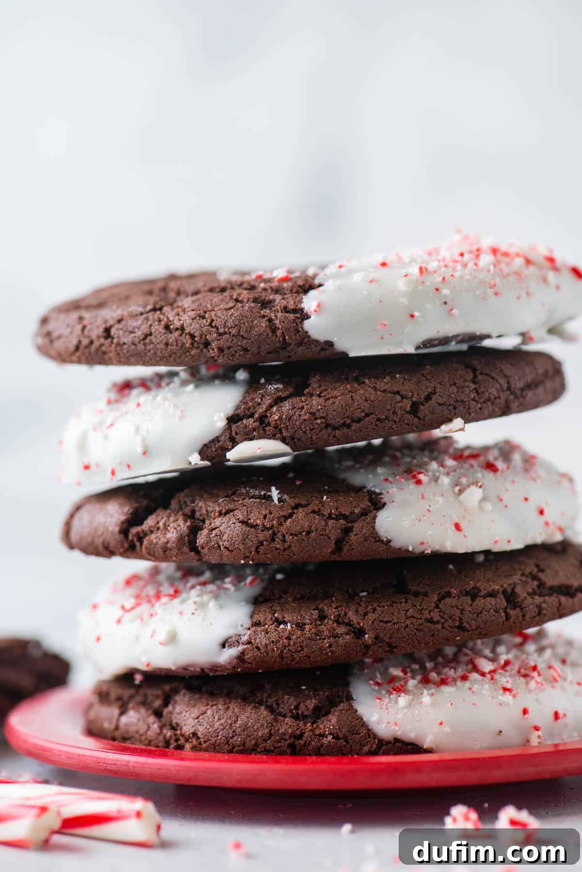 These Chocolate Candy Cane Cookies feature soft, chewy chocolate cookies dipped in white chocolate and sprinkled with crushed candy canes. A perfectly stacked pile of chocolate candy cane cookies, showcasing their uniform size and inviting appearance.