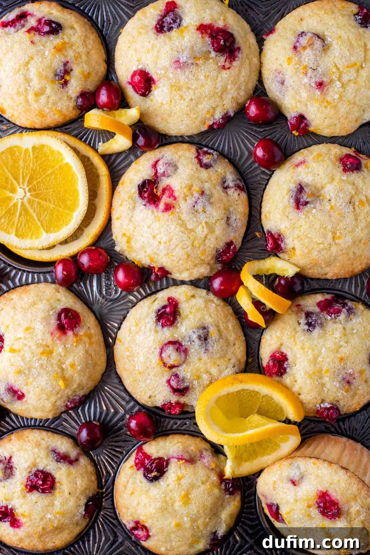 Overhead view of perfectly baked bakery-style cranberry orange muffins, arranged on a cooling rack with fresh orange slices and cranberries.
