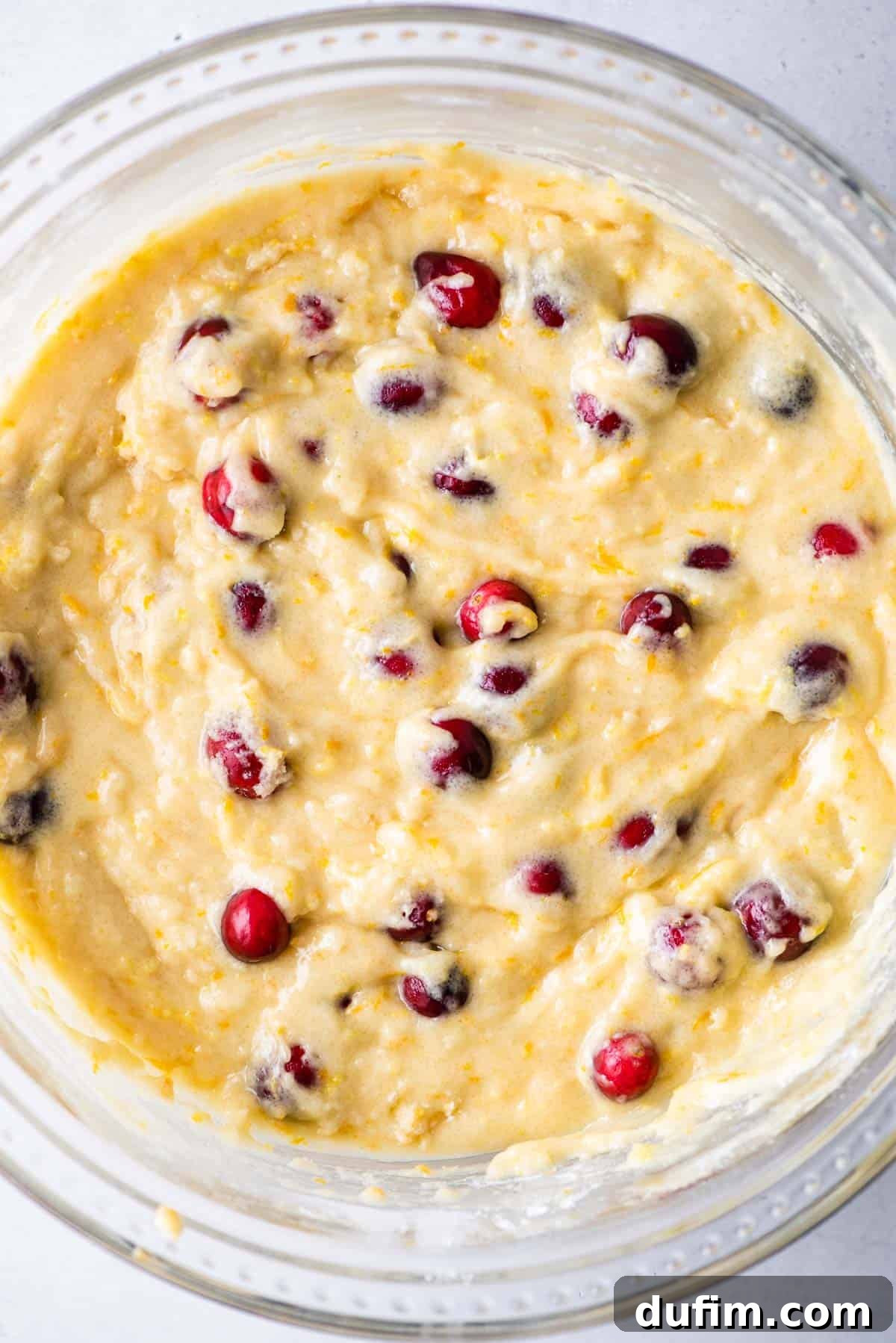 Thick, vibrant orange cranberry muffin batter in a mixing bowl, ready for the resting period.