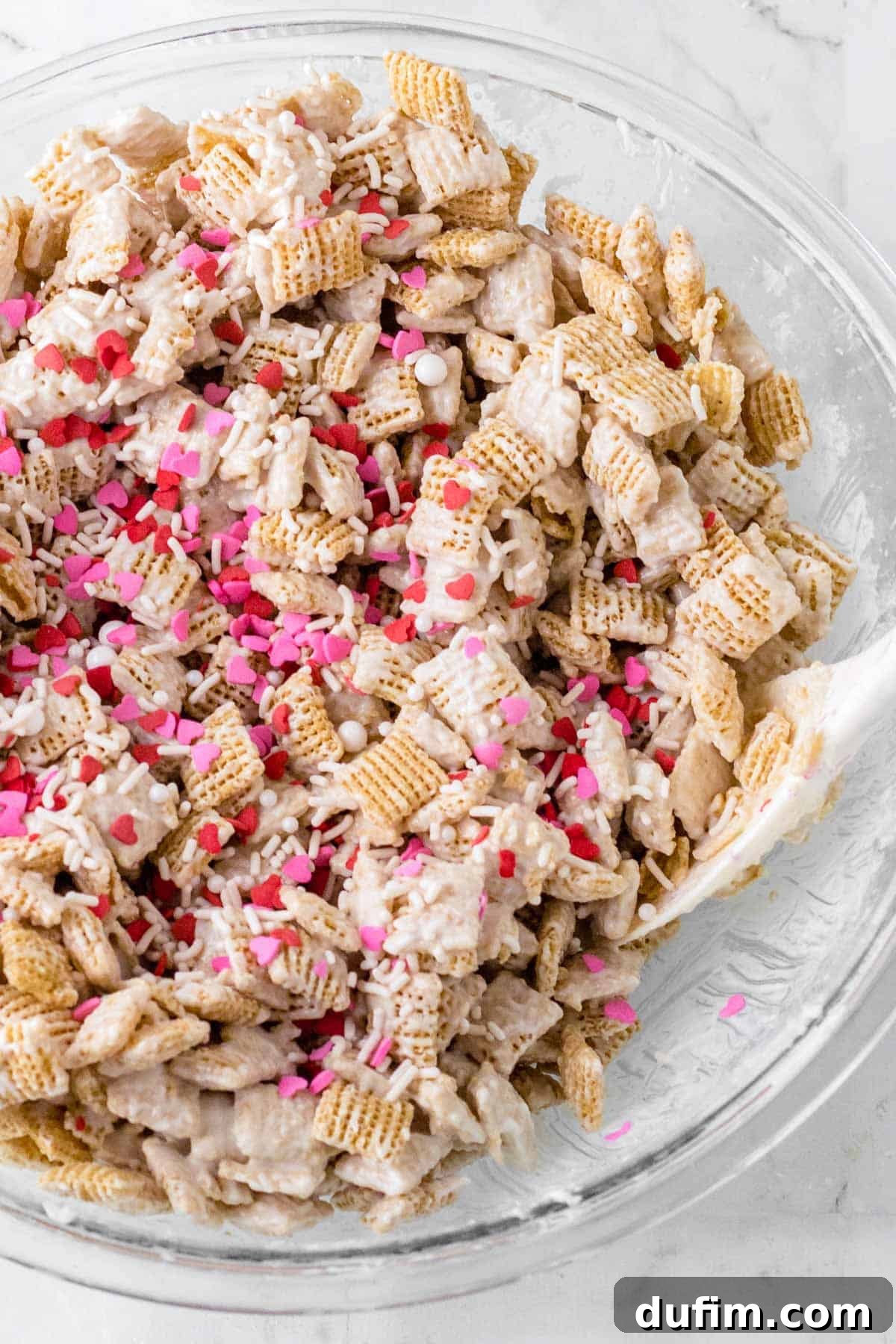 Valentine's Day Puppy Chow recipe in a clear bowl sitting on a white countertop