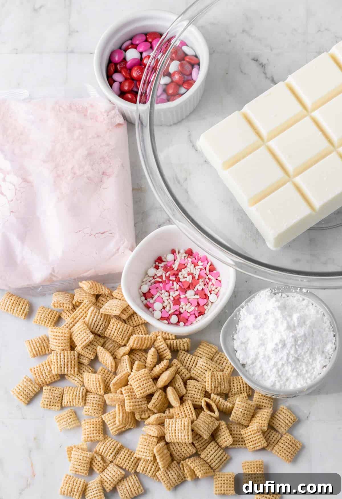Ingredients for Valentine's day puppy chow in separate bowls including Rice Chex cereal, White almond bark, Strawberry cake mix, Powdered sugar, and Valentine’s Day Sprinkles and Valentine’s Day M&Ms