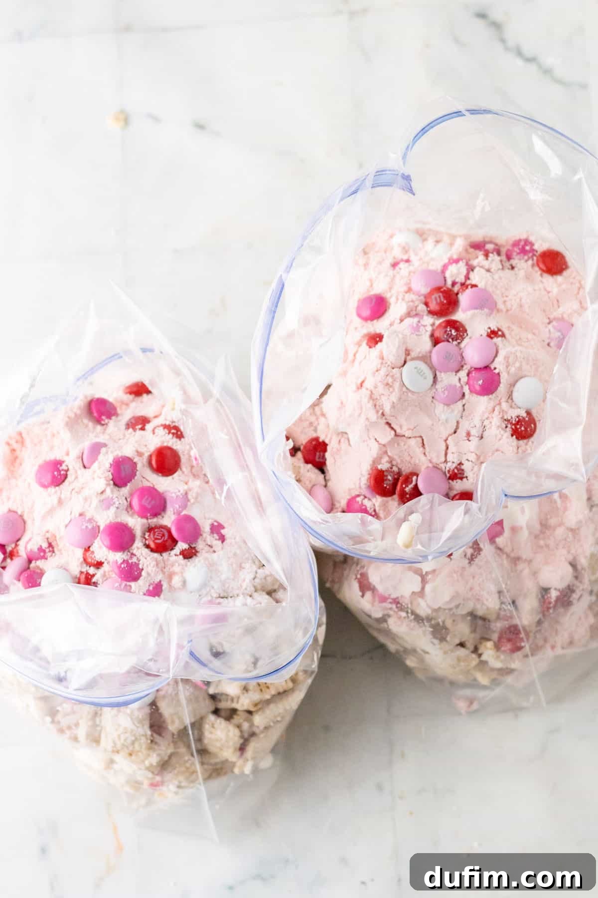 Valentine's Day Puppy Chow mixture inside large plastic bags sitting on a white counter.