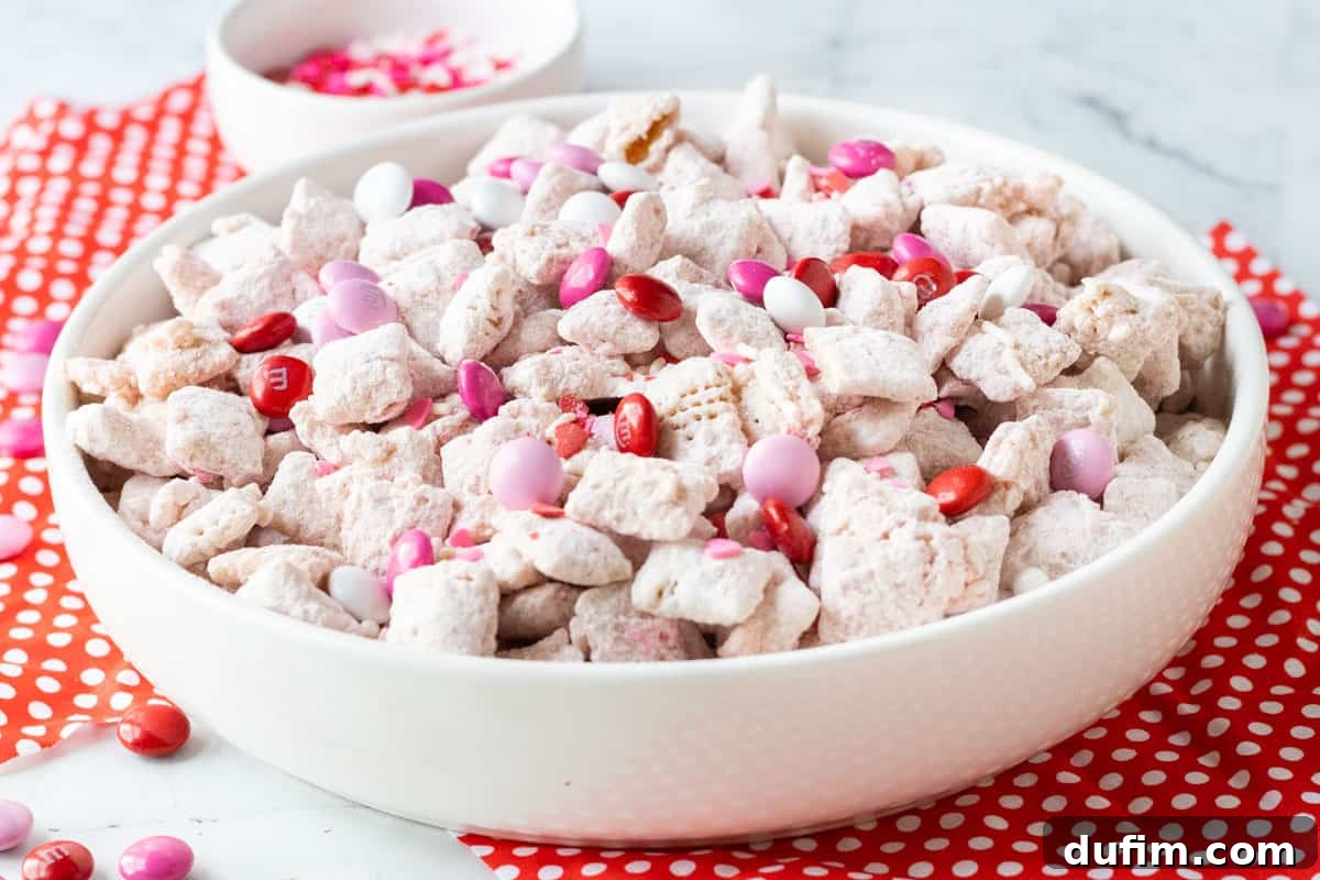 Valentine's Day Puppy Chow in a white bowl sitting on top of a white counter and red napkins with white polka dots on them.