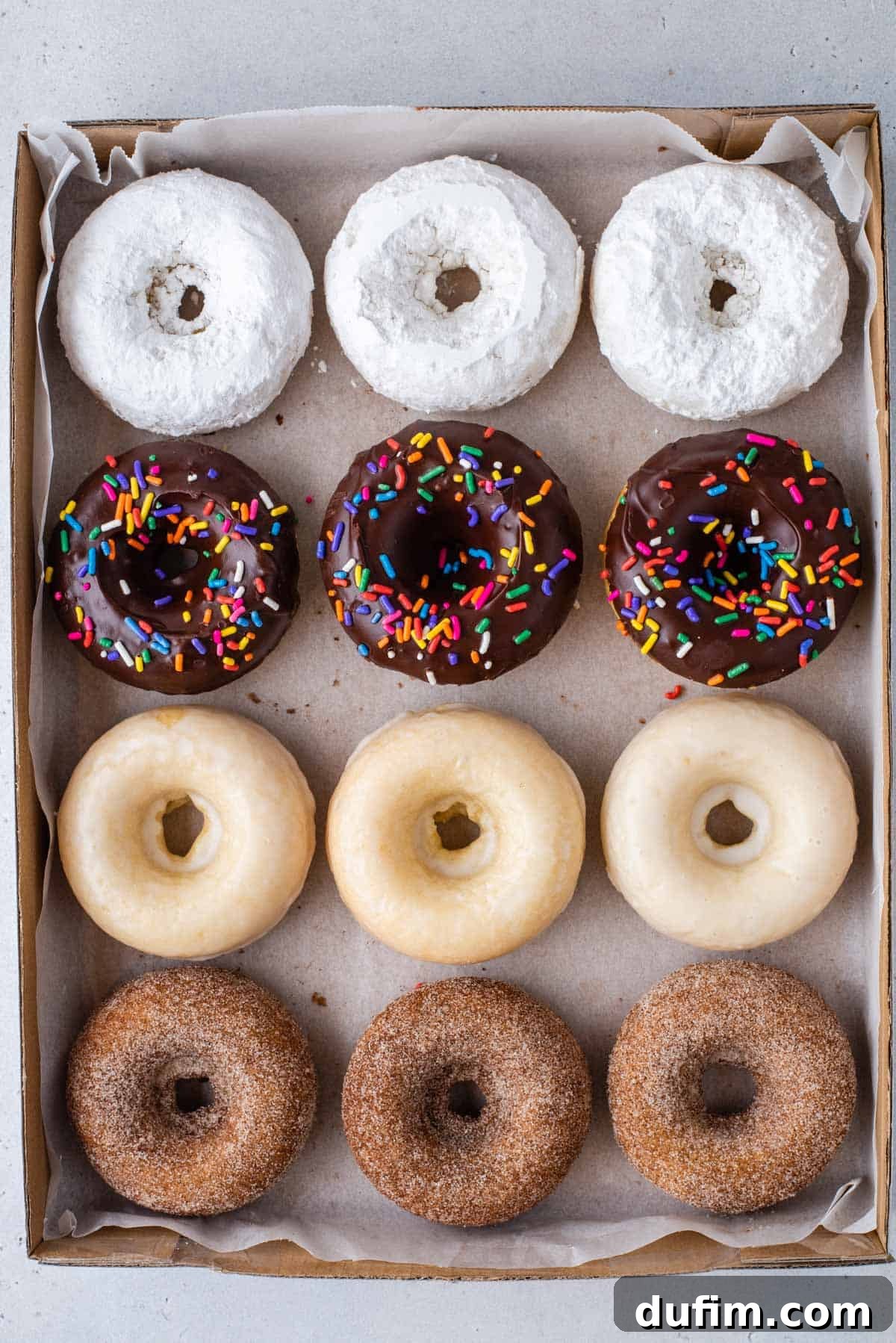 An array of powdered sugar, chocolate glazed, Krispy Kreme glazed, and cinnamon sugar gluten free donuts on a baking sheet