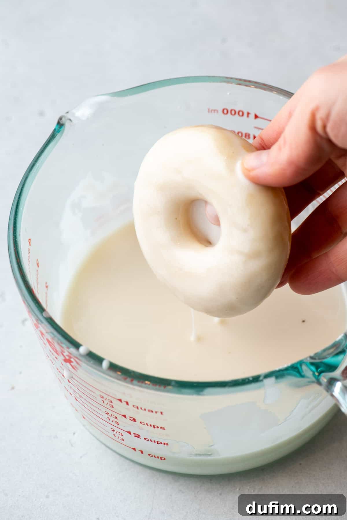 A hand dipping a baked gluten free donut into a smooth white glaze