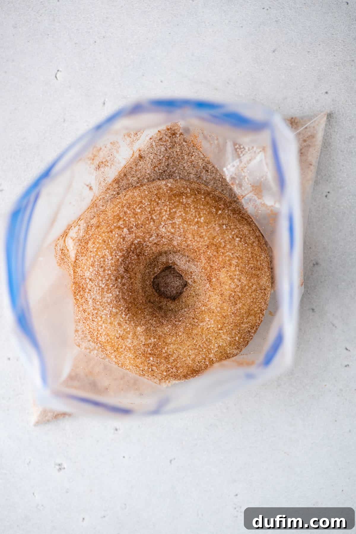 A baked gluten free donut being tossed with cinnamon sugar in a ziploc bag