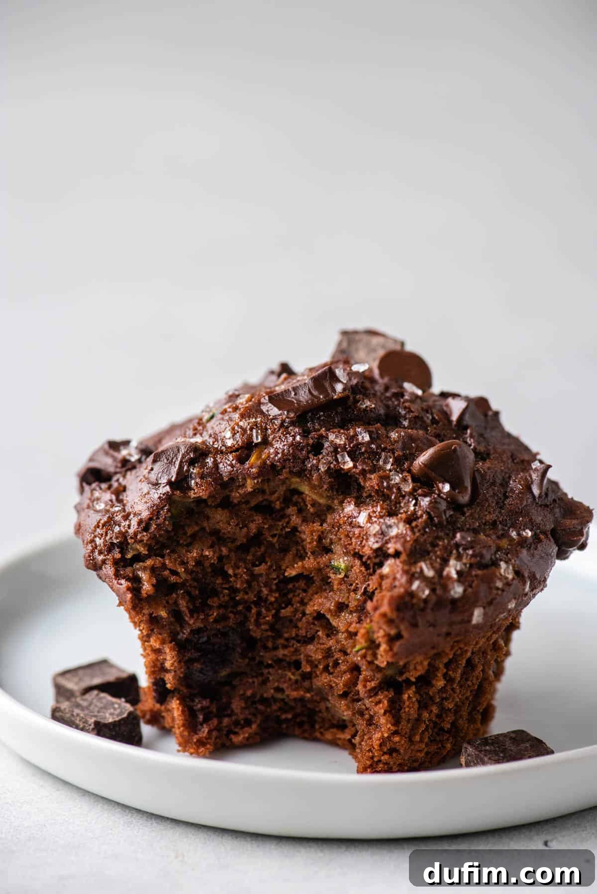 These Chocolate Zucchini Muffins are rich, moist, and oh-so-good. The zucchini adds moisture while cocoa powder adds chocolate decadence. A chocolate zucchini muffin with a portion bitten off, revealing a soft, fluffy texture and rich chocolate distribution.