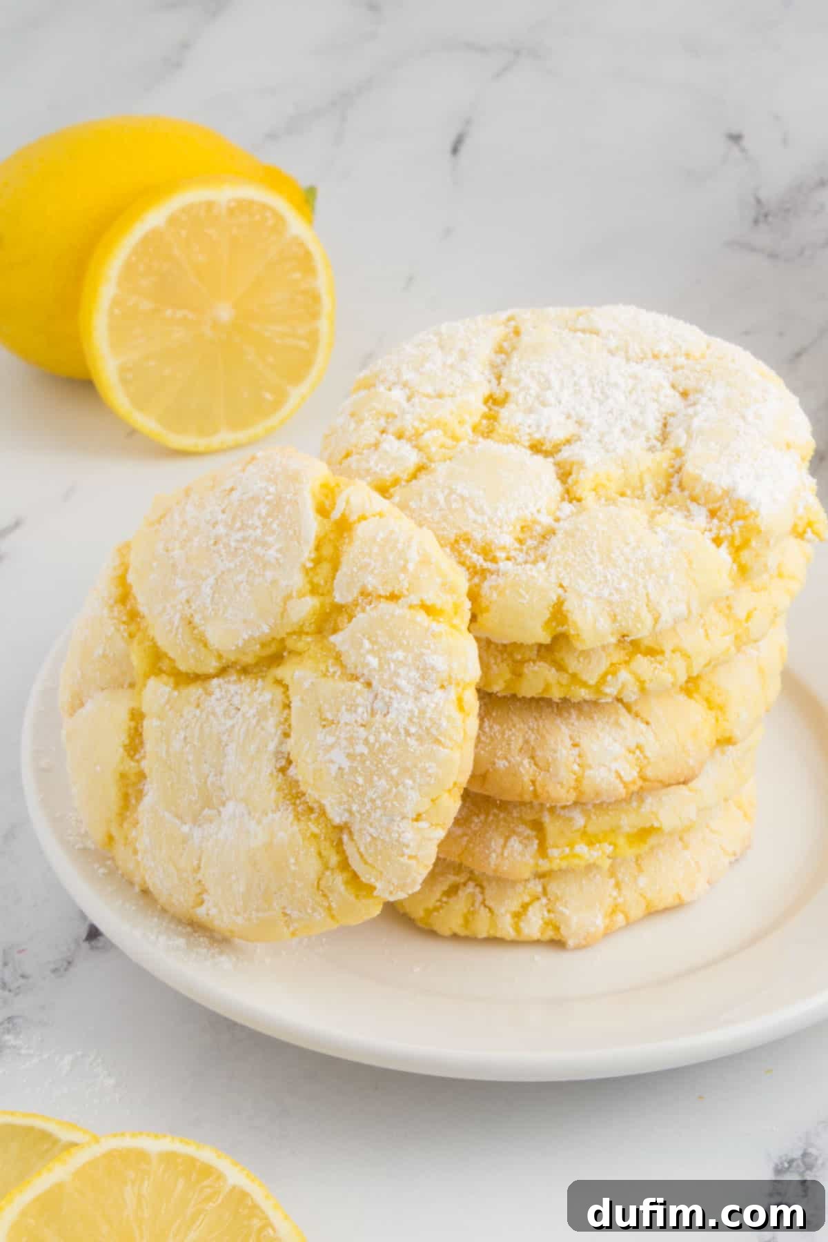 Beautifully arranged lemon cookies on a white plate, surrounded by fresh lemon slices and green mint leaves on a granite countertop, ready for serving.