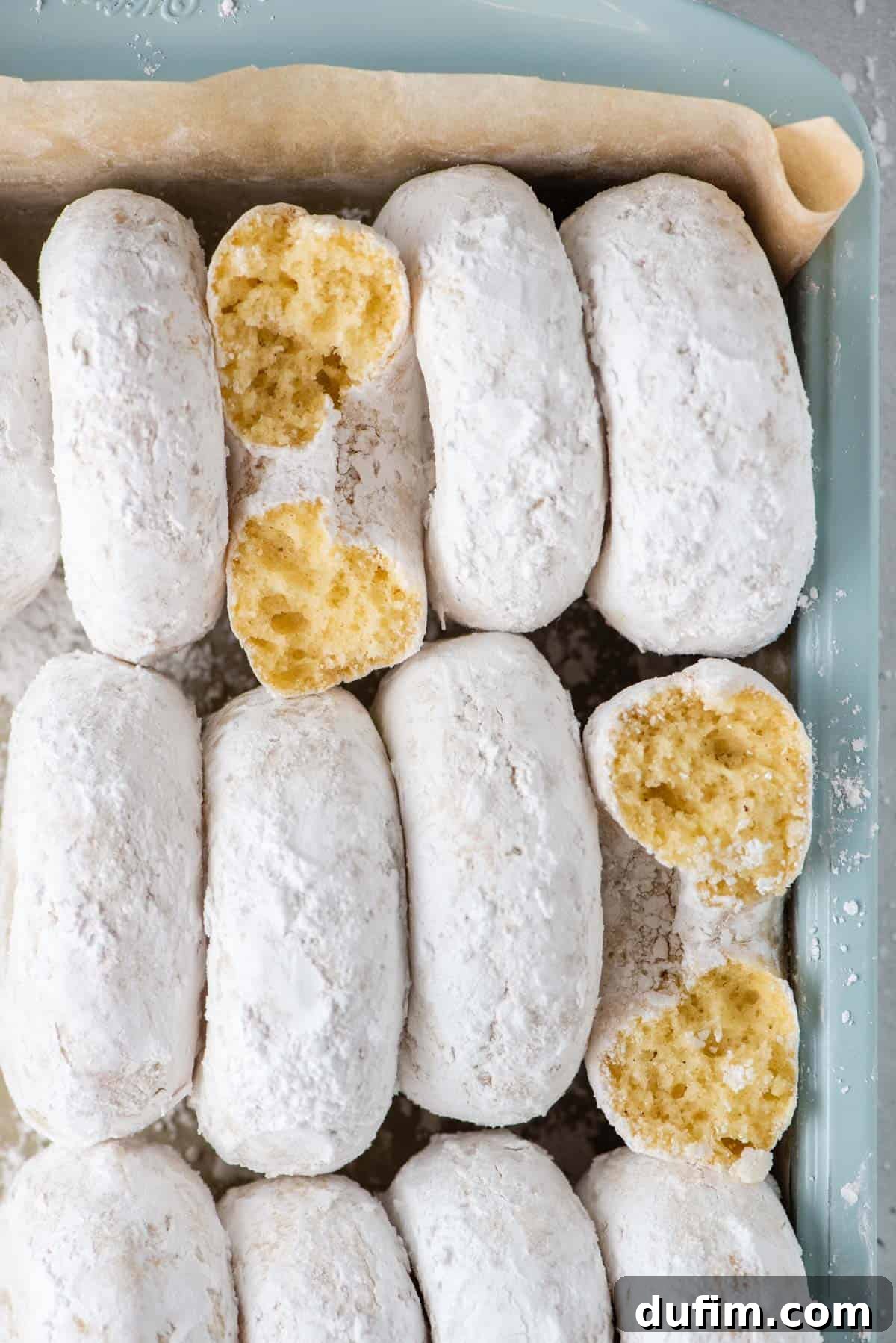 Powdered Sugar Donuts arranged neatly, standing vertically side-by-side in a teal baking dish lined with brown paper, ready to be served.