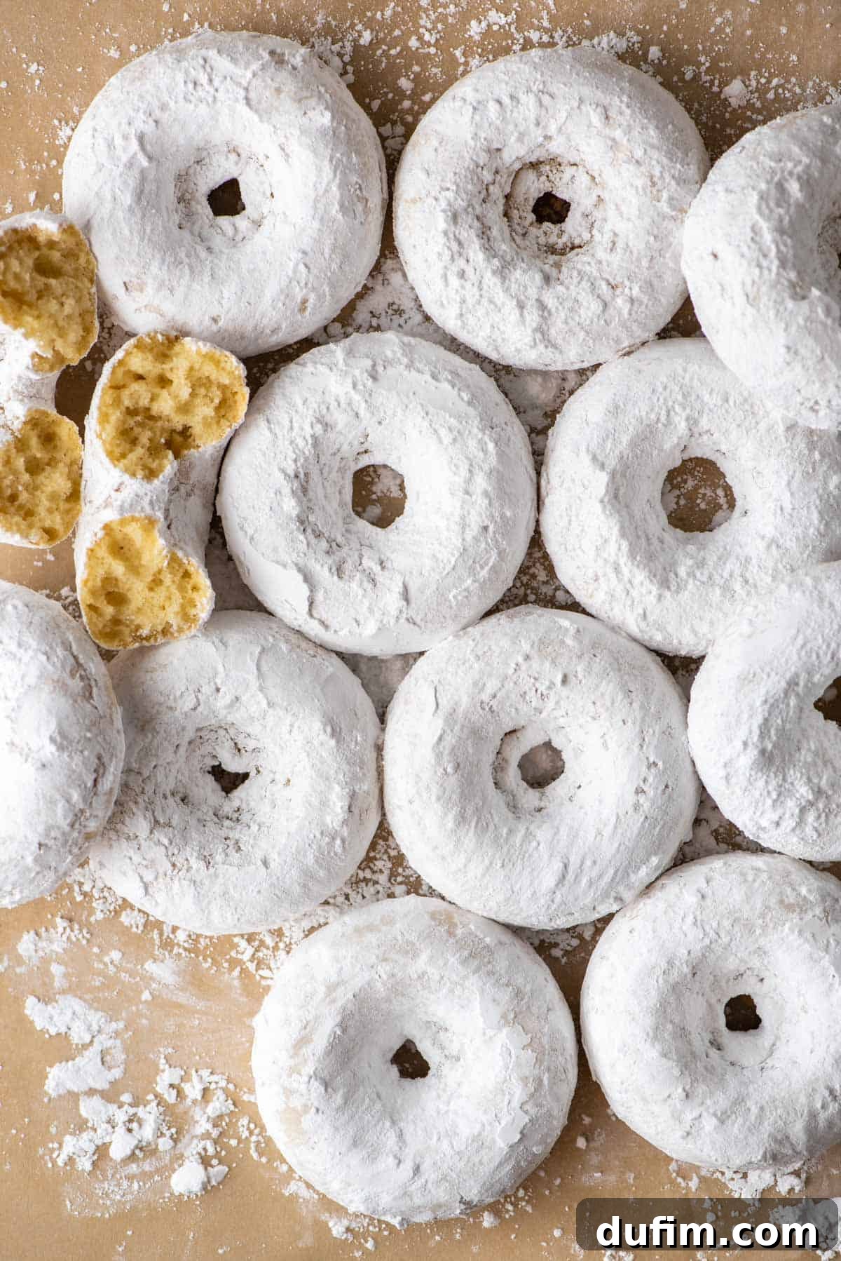 A selection of baked powdered sugar donuts casually arranged on brown paper, emphasizing their homemade charm and inviting presentation.