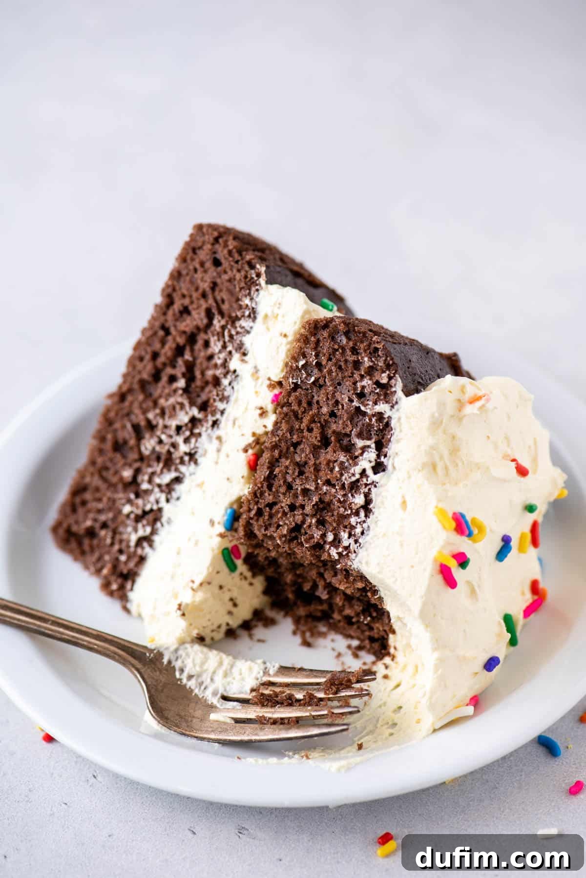 partially eaten chocolate cake topped with cool whip frosting and sprinkles on a white plate with a fork