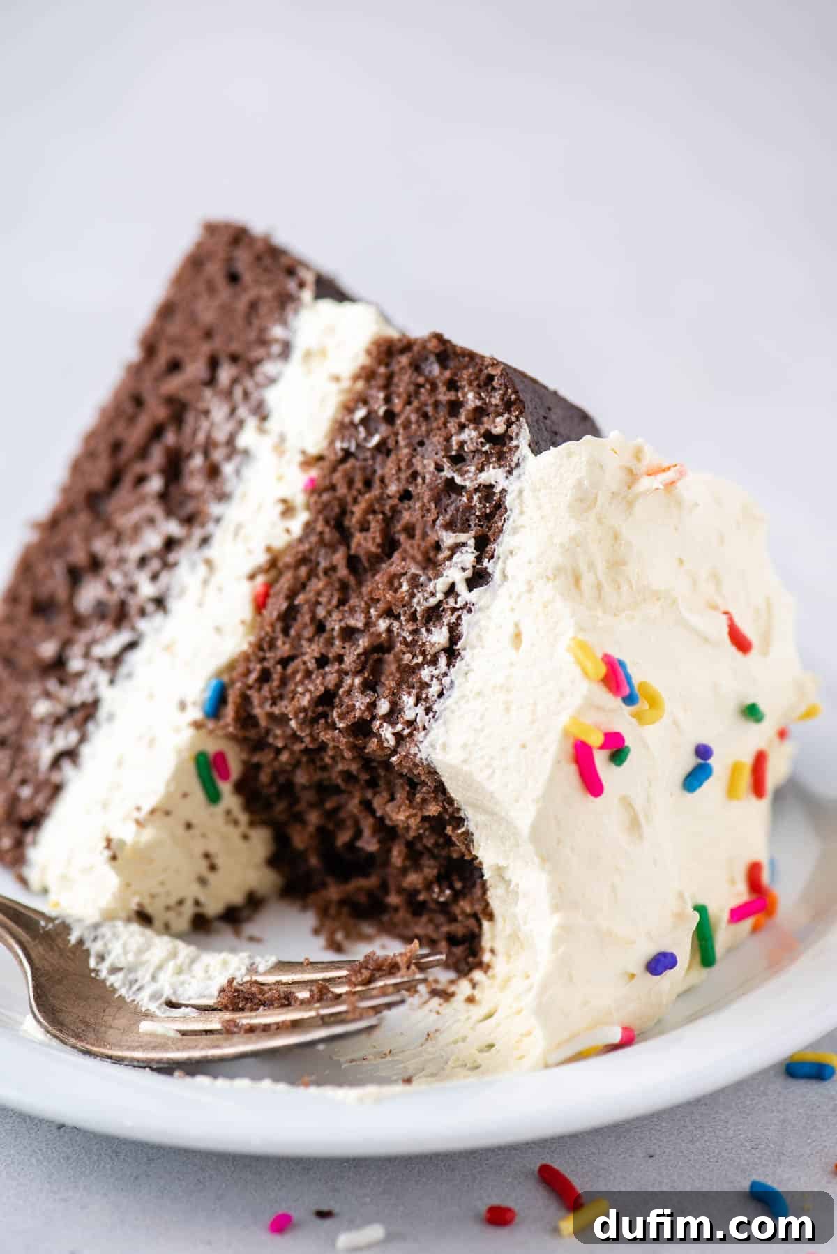 partially eaten chocolate cake topped with cool whip frosting and sprinkles on a while plate with a fork