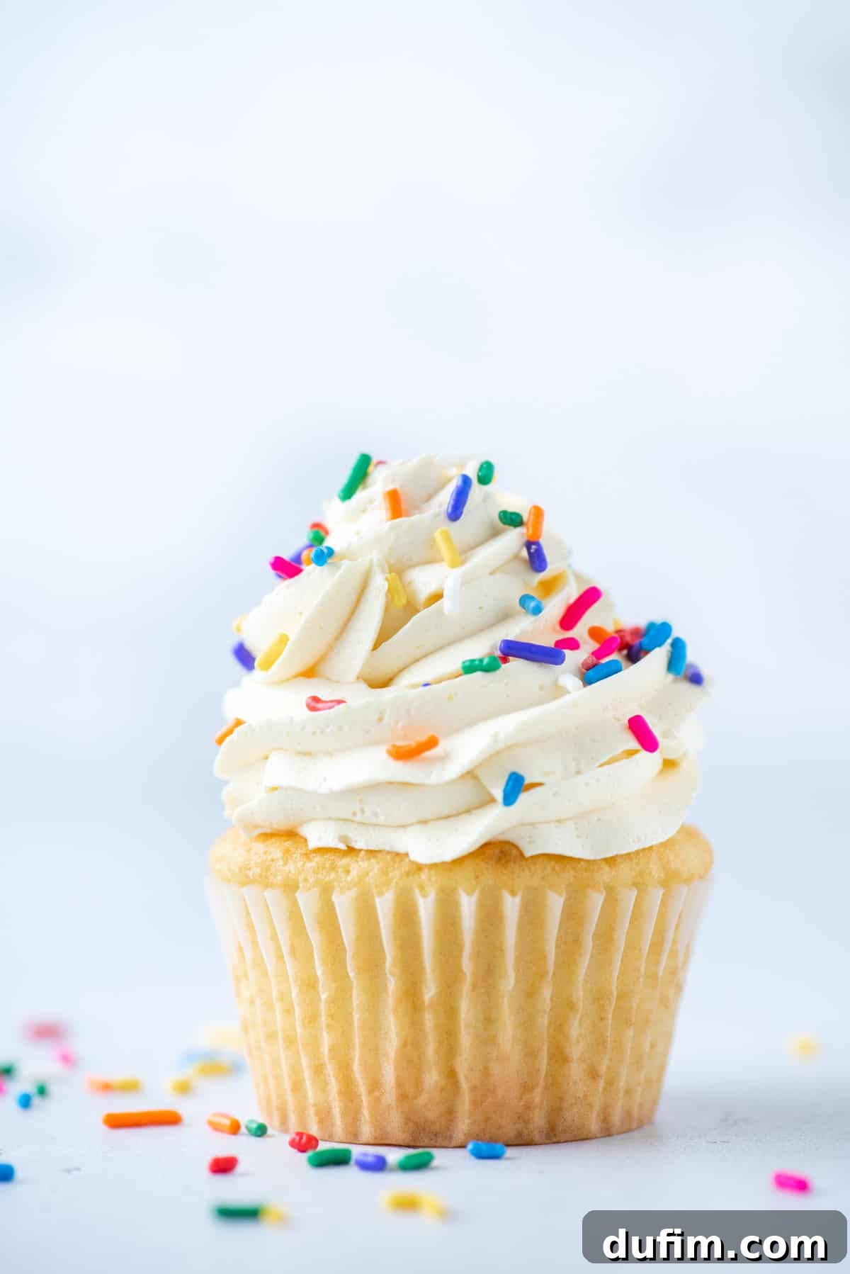 vanilla cupcake topped with cool whip frosting and sprinkles with sprinkles around it on a white surface