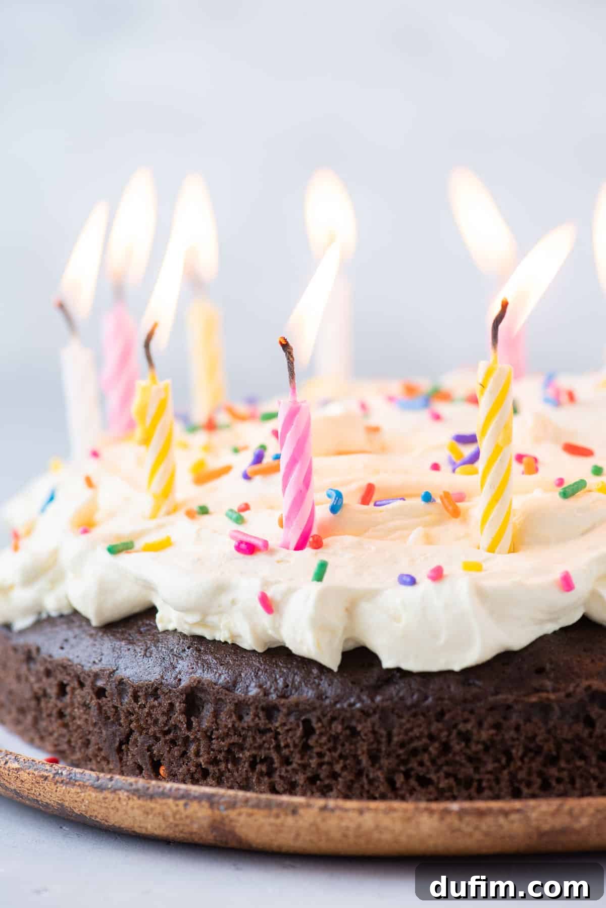 chocolate cake topped with cool whip frosting with sprinkles and lit birthday candles on top