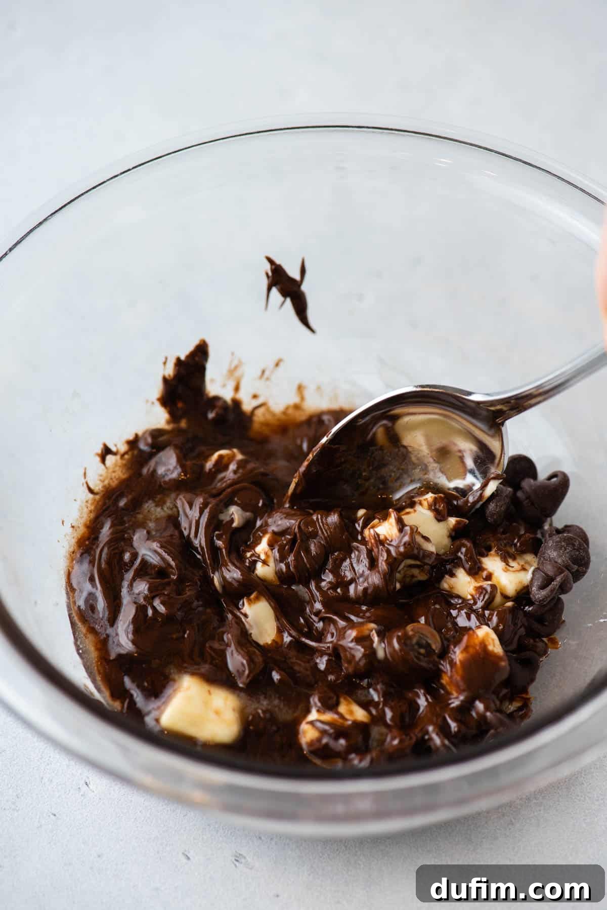The melted mixture of chocolate chips, butter, and corn syrup, perfectly combined into a smooth, glossy chocolate glaze, ready for use in a clear glass bowl.