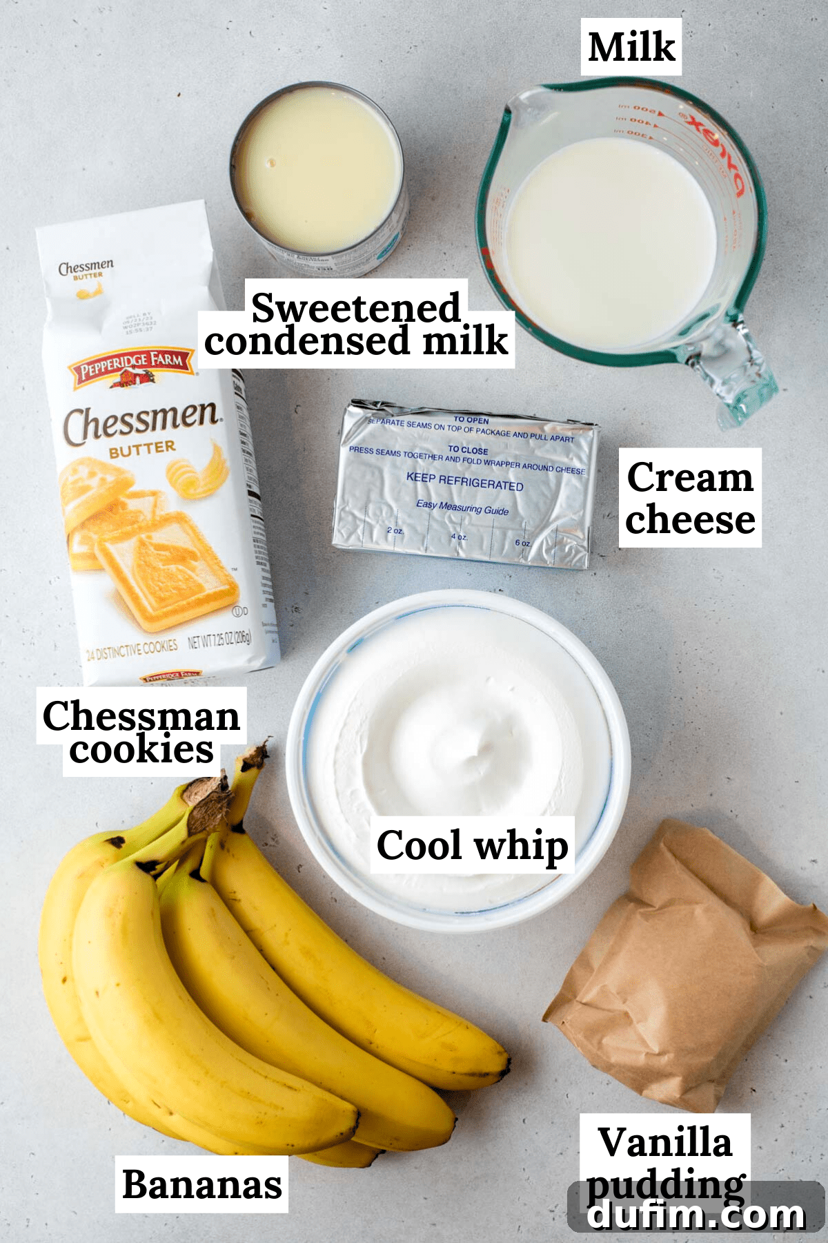 Ingredients for banana pudding laid out on a white countertop, including Chessmen cookies, Cool Whip, instant vanilla pudding mix, fresh bananas, milk, sweetened condensed milk, and cream cheese.